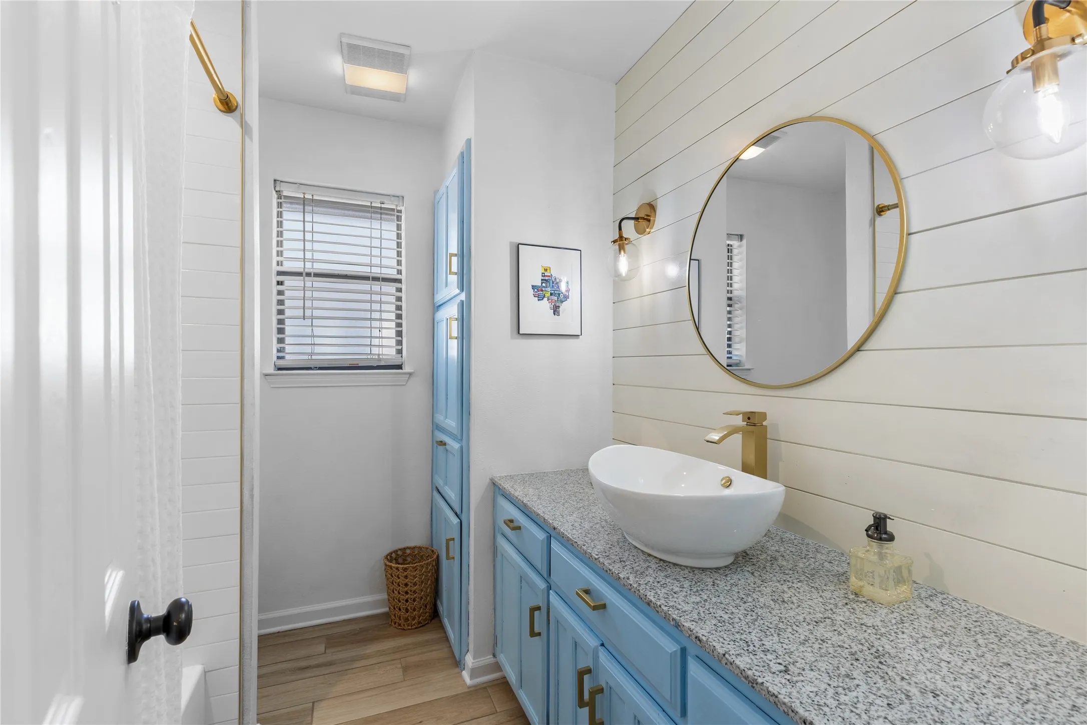 Bathroom featuring a vessel sink, gold-tone fixtures, wood-finish flooring, a built-in storage cabinet, and a shiplap accent wall