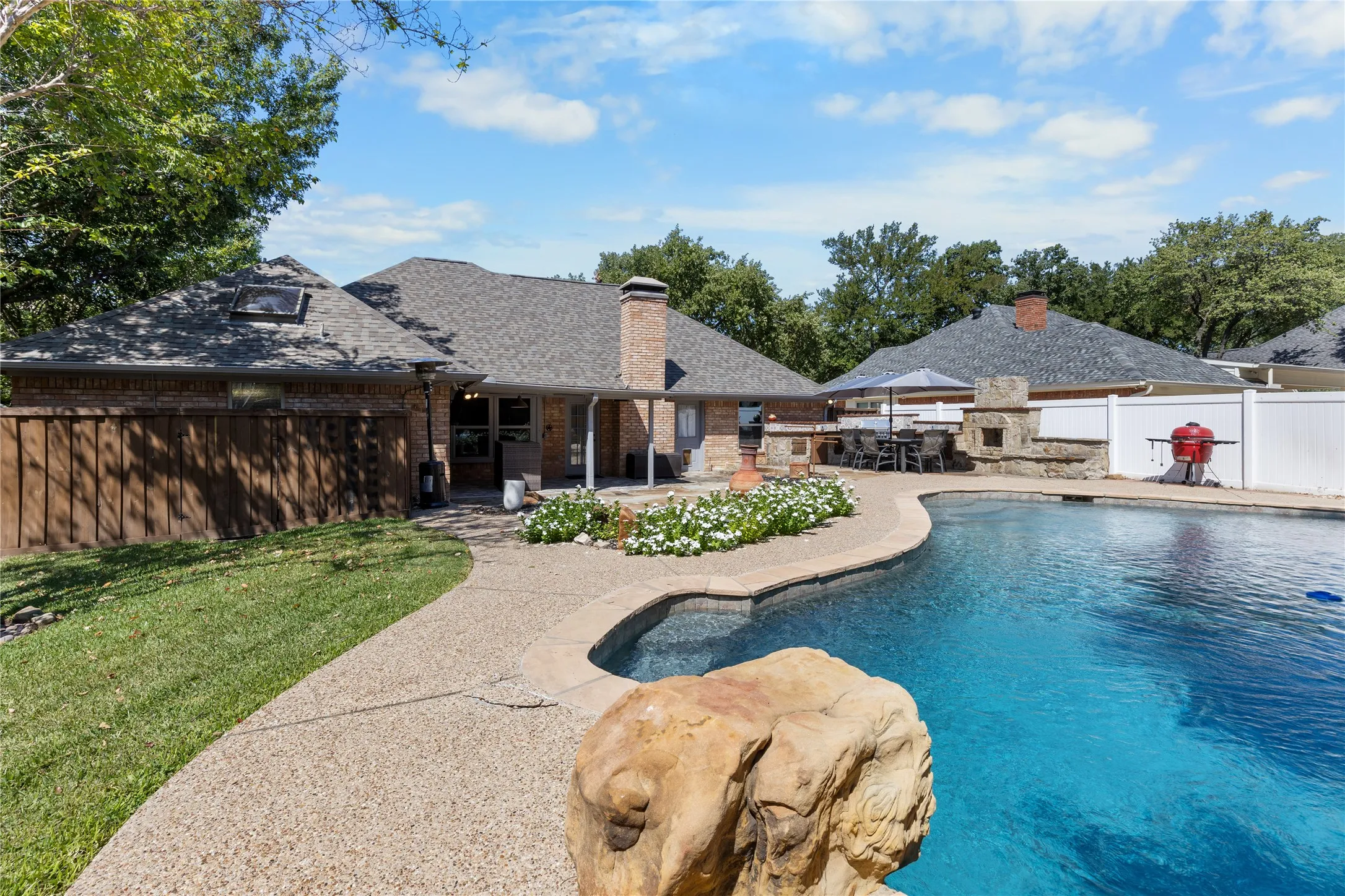 Expansive backyard featuring a curved swimming pool, a built-in outdoor kitchen with stone detailing, a stone fireplace, and a manicured lawn