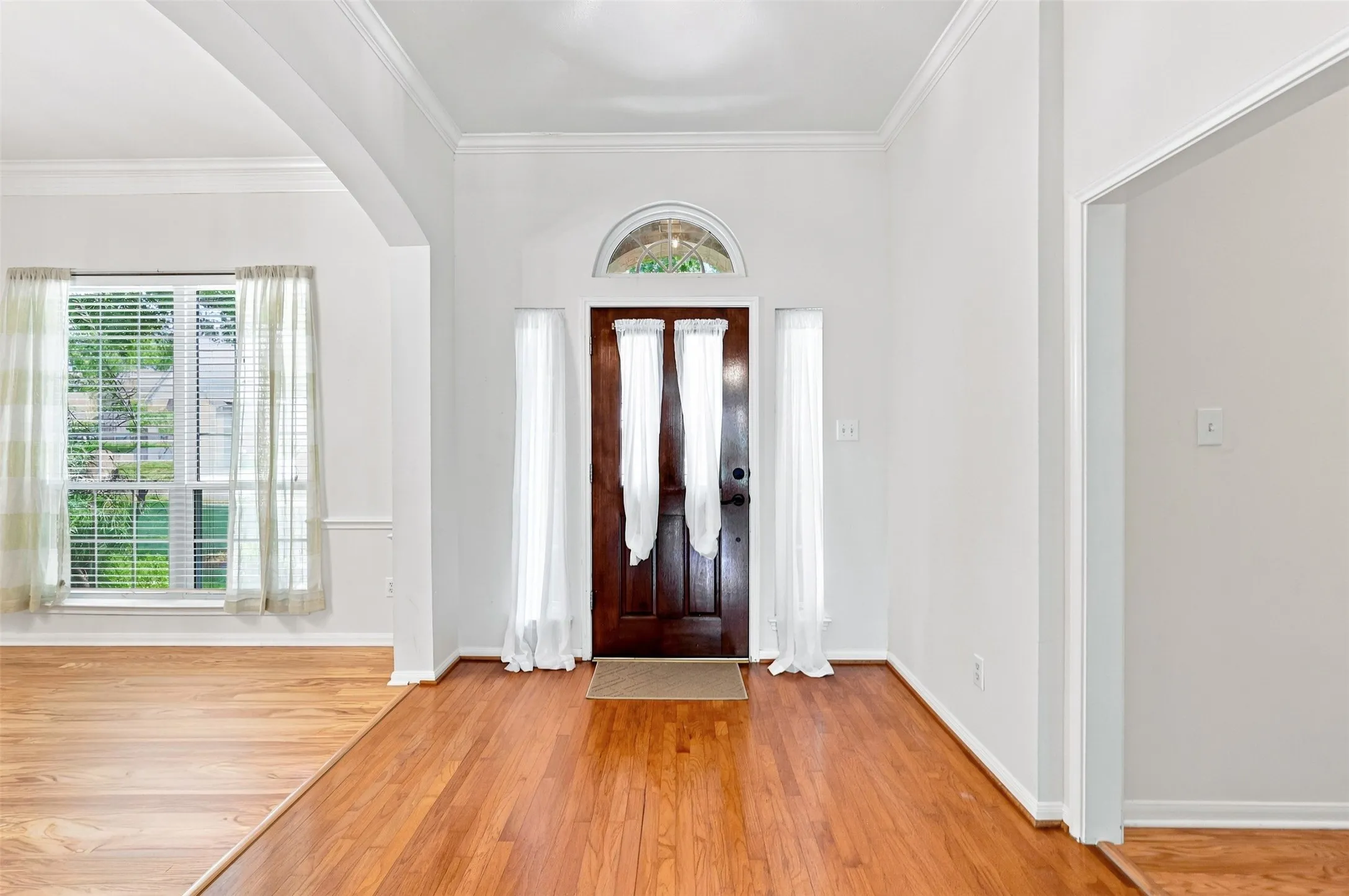 Entryway featuring wood-finish flooring, a wood paneled door with an arched transom, and white wall finishes.