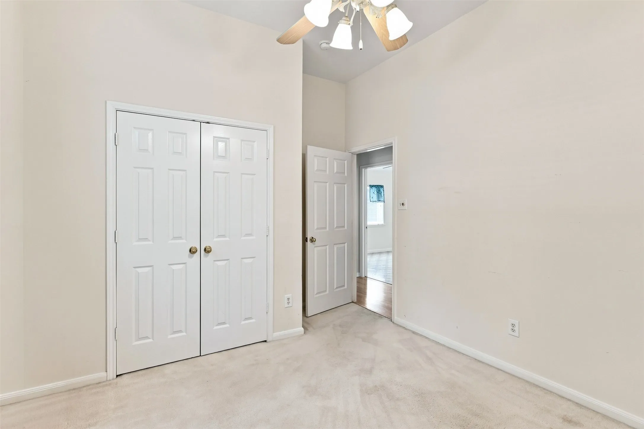 Vaulted ceiling with a ceiling fan, white paneled bifold closet doors, and light-colored wall-to-wall carpeting