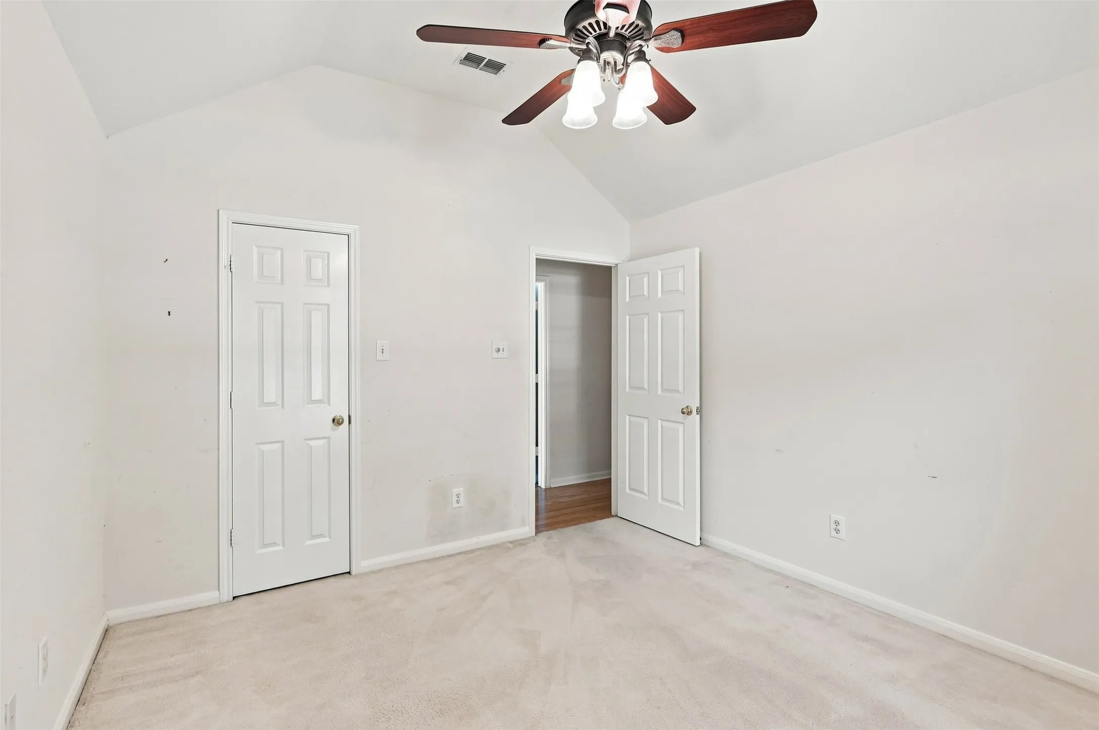 Vaulted ceiling, ceiling fan with integrated lighting, paneled interior doors, and carpet flooring