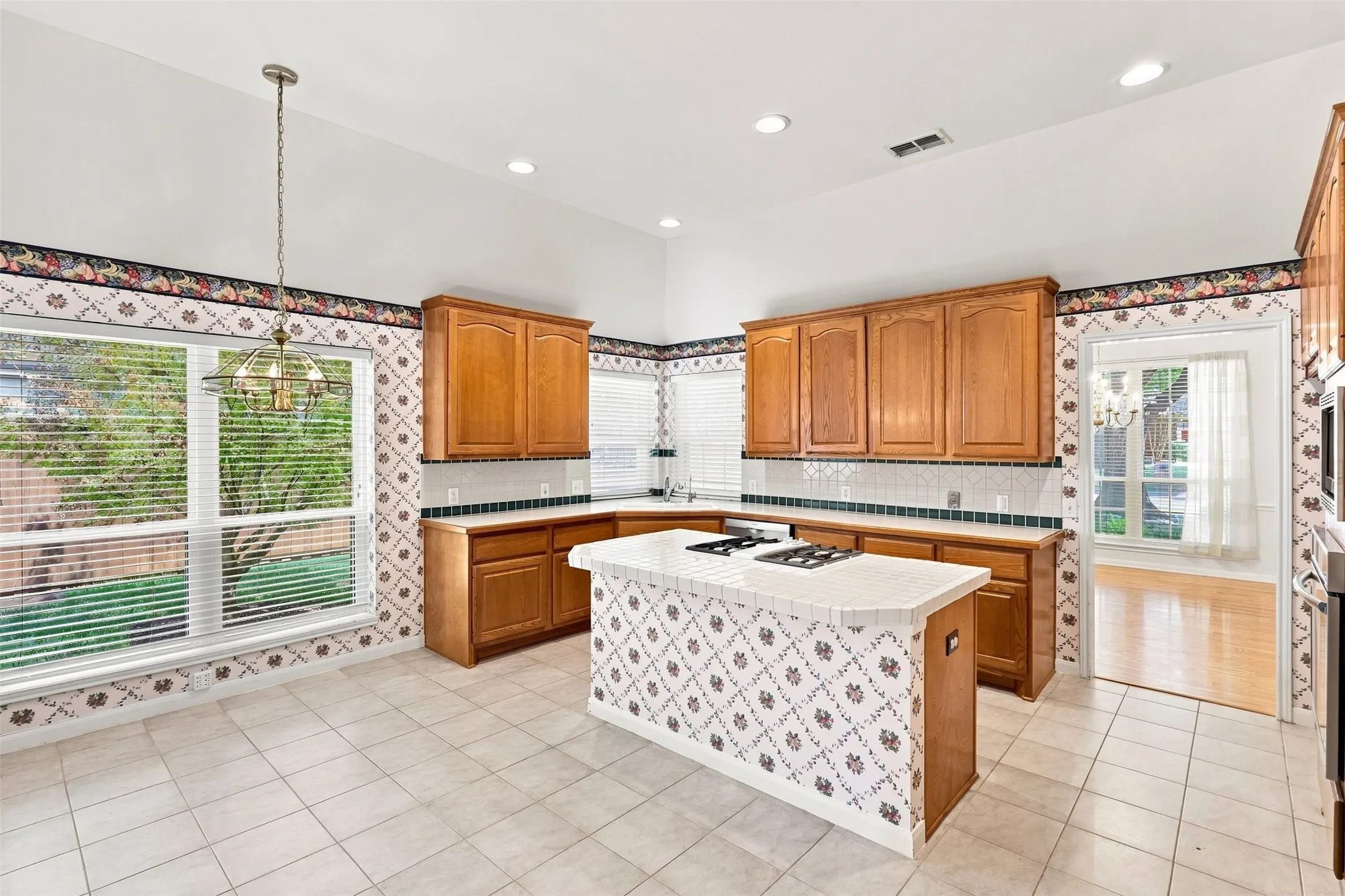 Kitchen featuring wood cabinetry, white tile flooring, a center island with a cooktop, and recessed lighting.