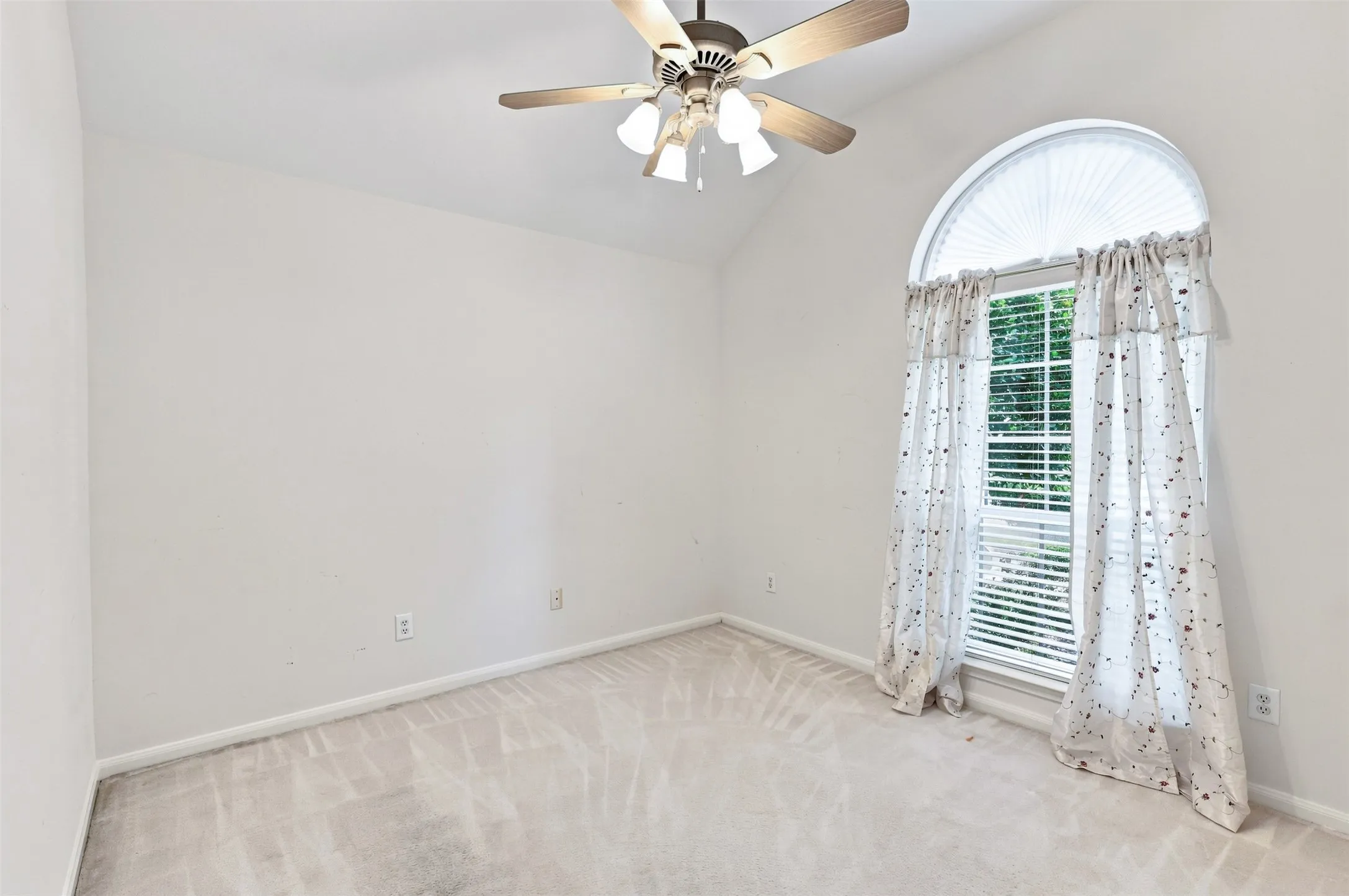 Secondary bedroom with vaulted ceiling with an attached ceiling fan, arched window with horizontal blinds, and neutral carpet flooring.