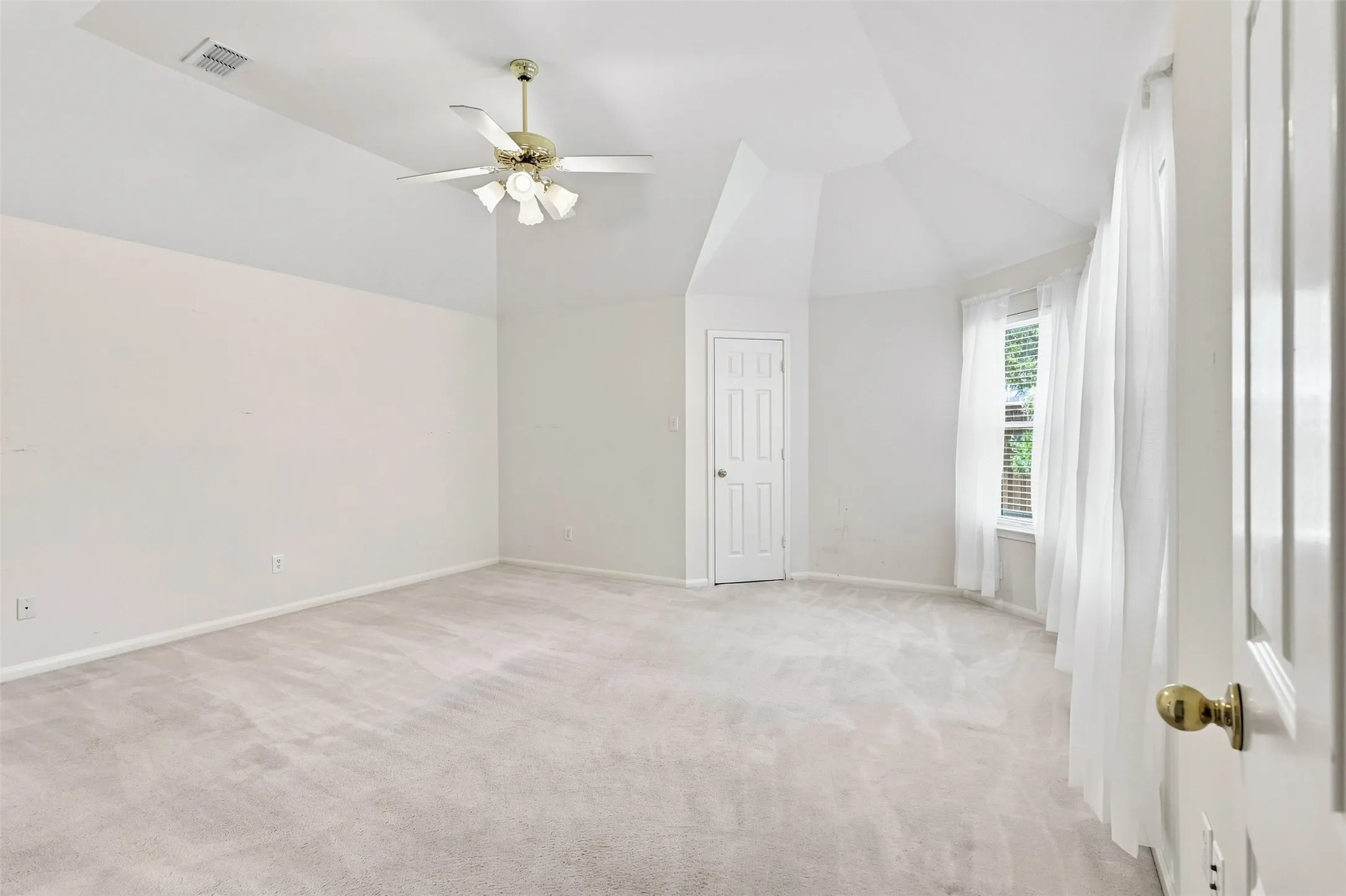 Primary bedroom features vaulted ceilings, carpeted flooring, ceiling fan with integrated lighting, paneled door, and a multi-pane window.