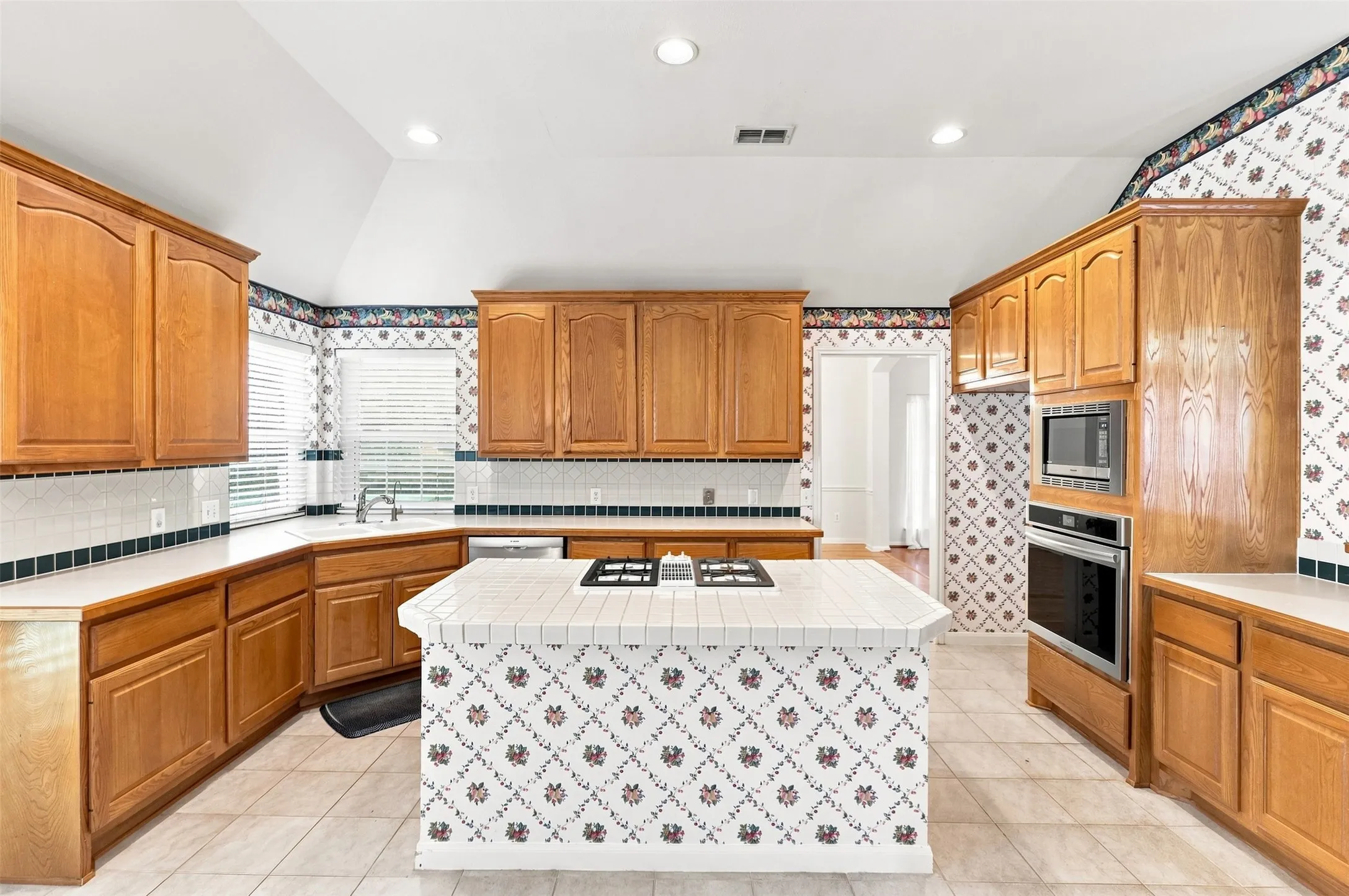 Kitchen featuring wood cabinetry, white tile countertops, a built-in oven, built-in microwave, and a center island with gas cooktop.