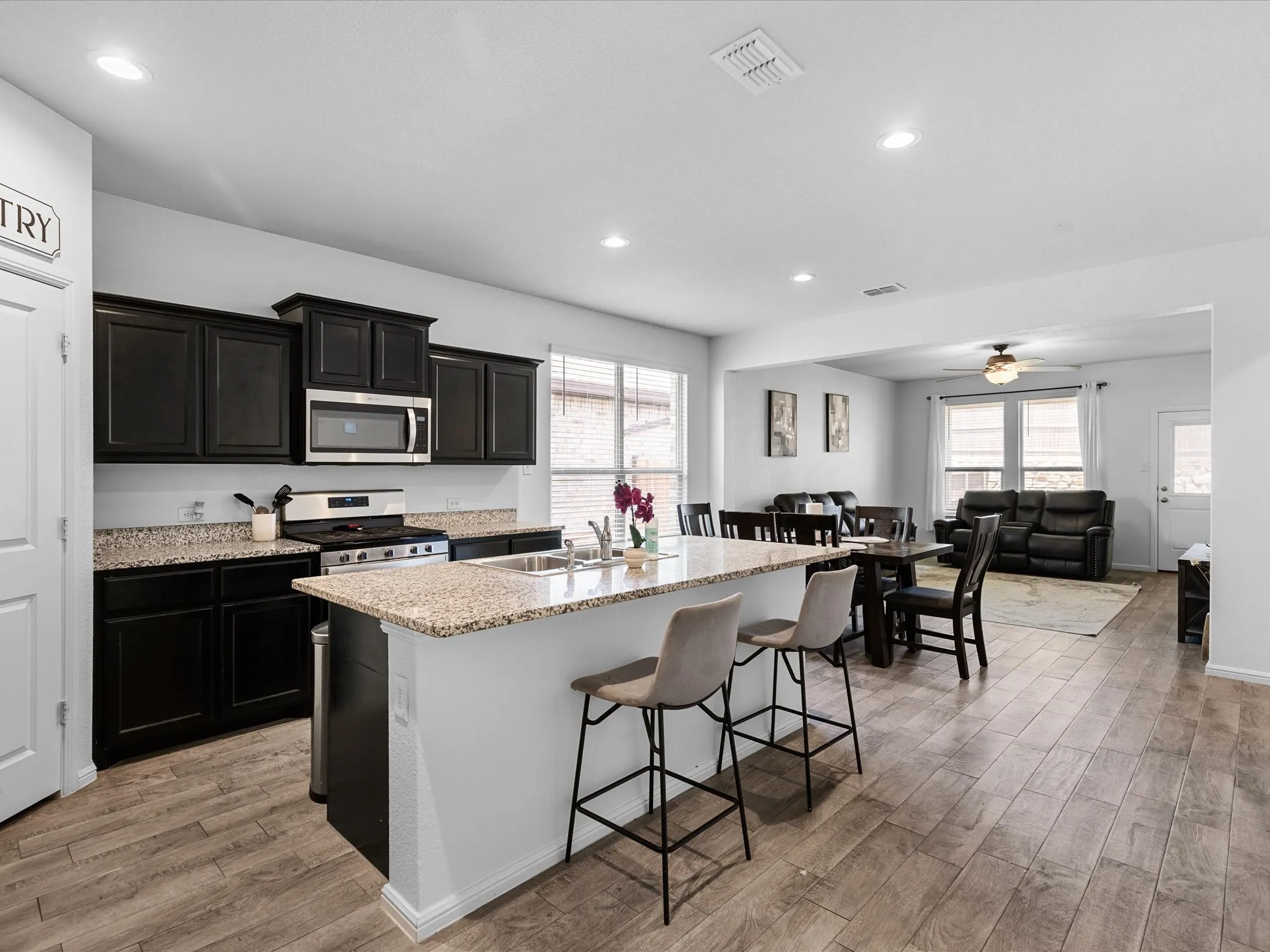 Kitchen island with a granite countertop, stainless steel appliances, dark wood-finish cabinetry, recessed lighting, and wood-finish flooring
