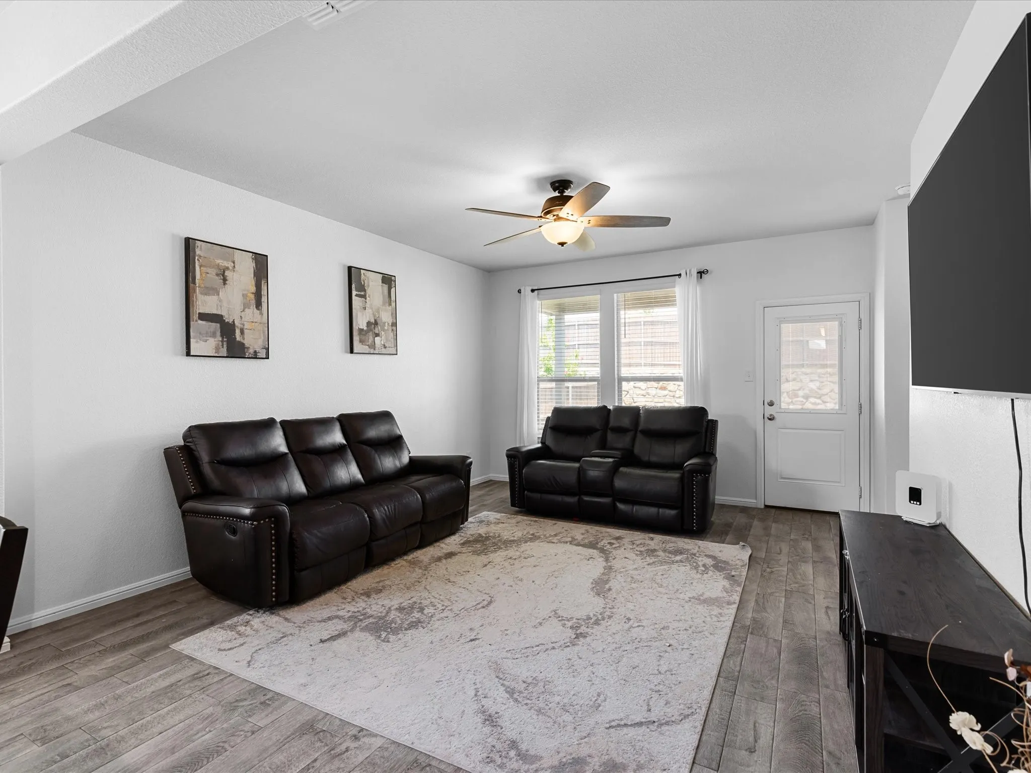 Spacious living area featuring wood-finish flooring, a ceiling fan with integrated lighting, and multiple windows with white blinds