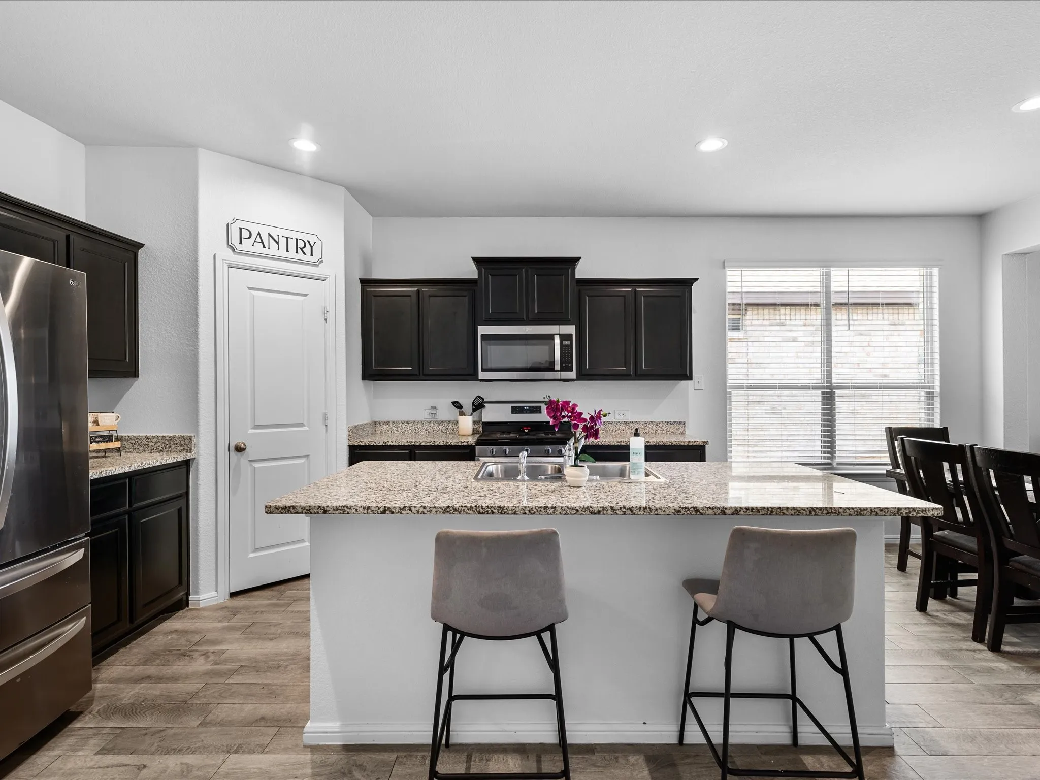 Kitchen featuring a center island, granite countertops, wood-finish flooring, dark wood cabinetry, and stainless steel appliances
