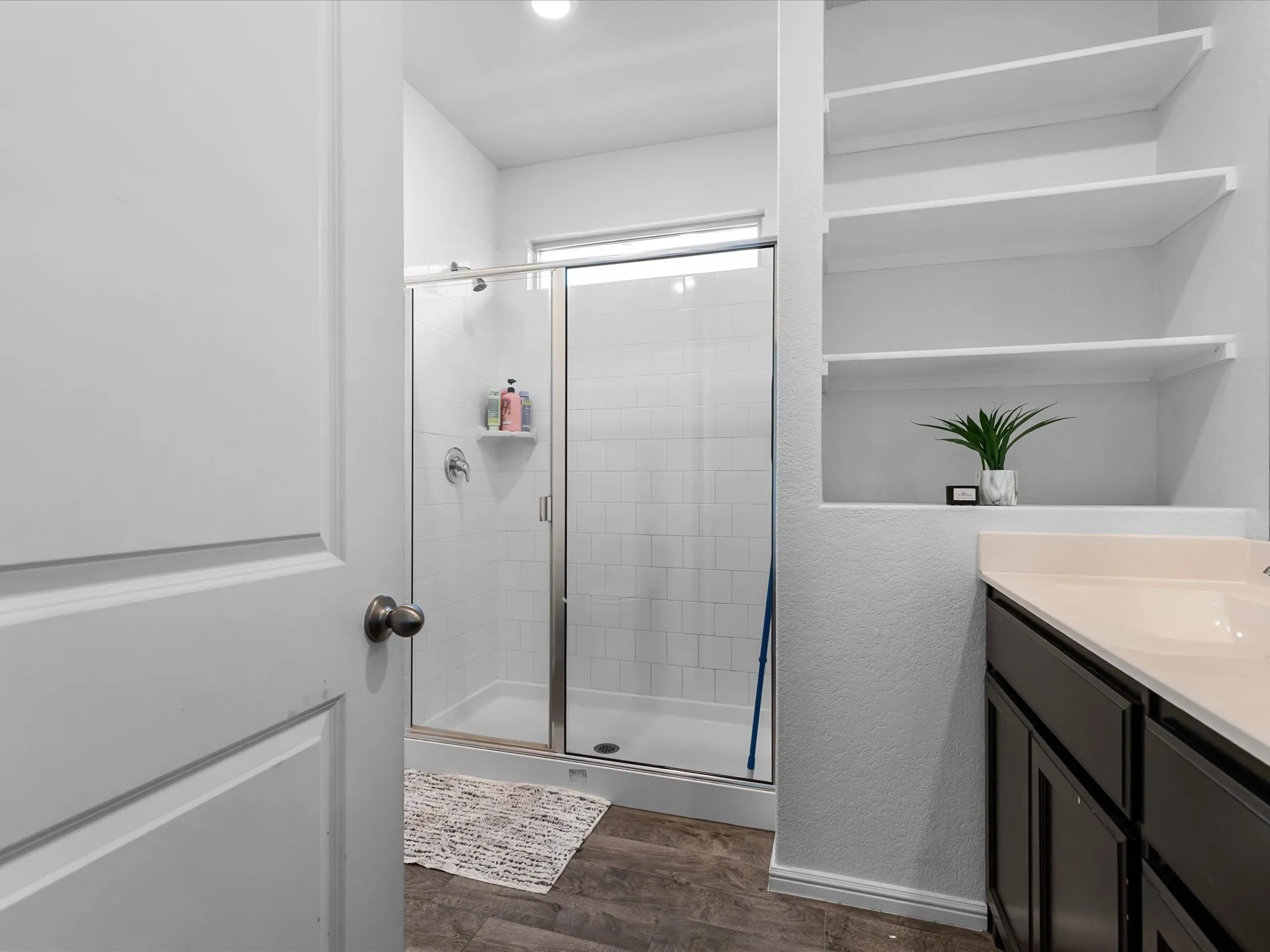 Glass-enclosed shower with white subway tile, a single vanity with dark cabinetry, integrated sink, and built-in shelving