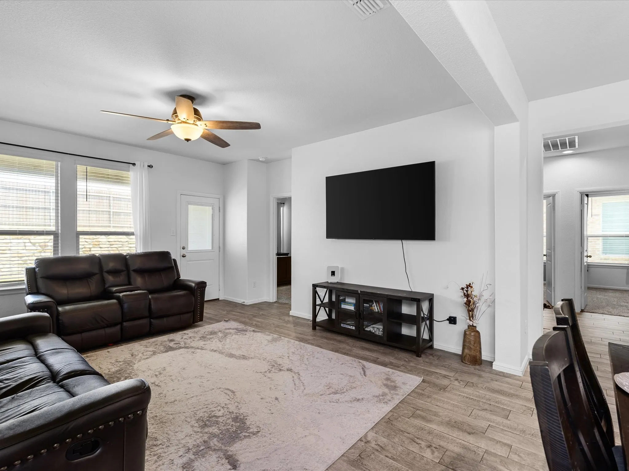 Spacious living area featuring wood-finish flooring, a ceiling fan, and multiple windows