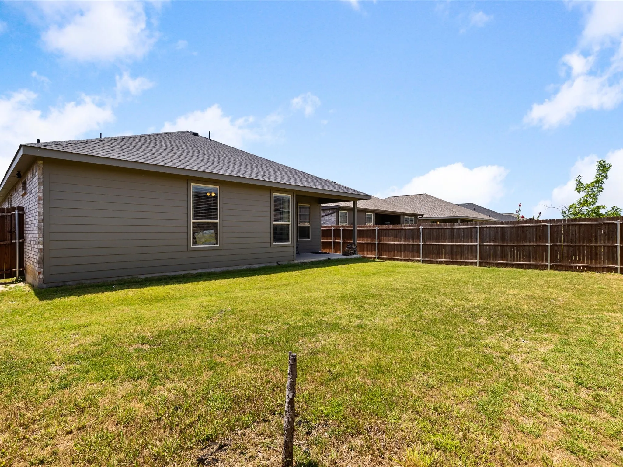Expansive grassy lawn with a wood plank privacy fence, siding exterior, brick accent wall, and a shingle roof