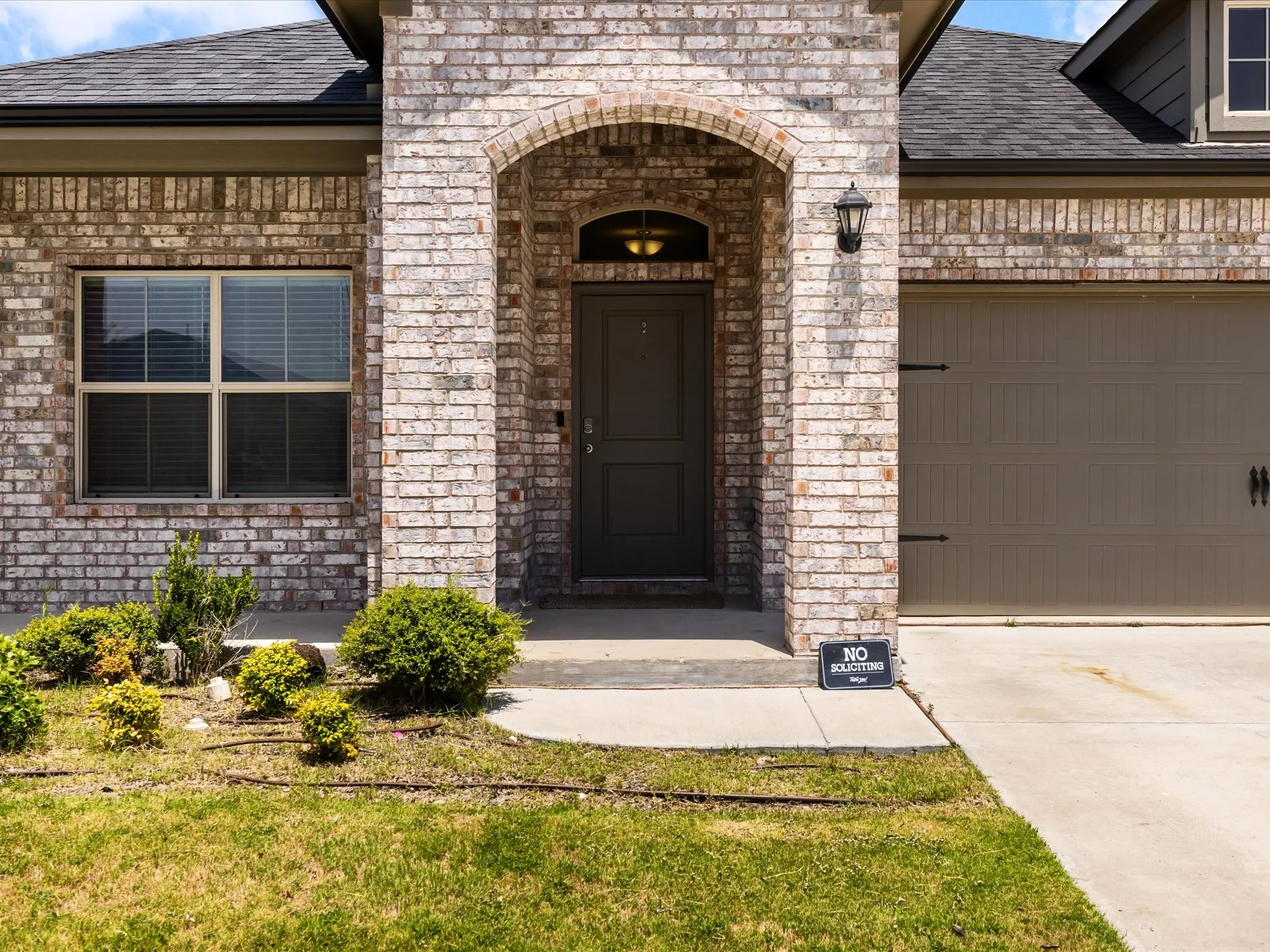 Brick exterior with an arched entryway, attached garage, and a landscaped front yard