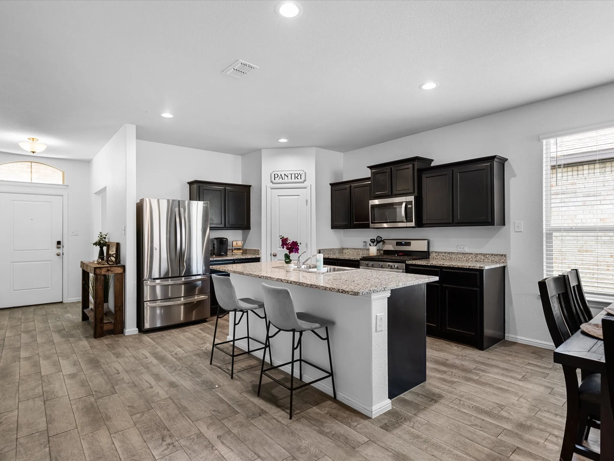 Kitchen featuring dark wood cabinetry, stainless steel appliances, a center island with bar seating, speckled countertops, and wood-finish flooring