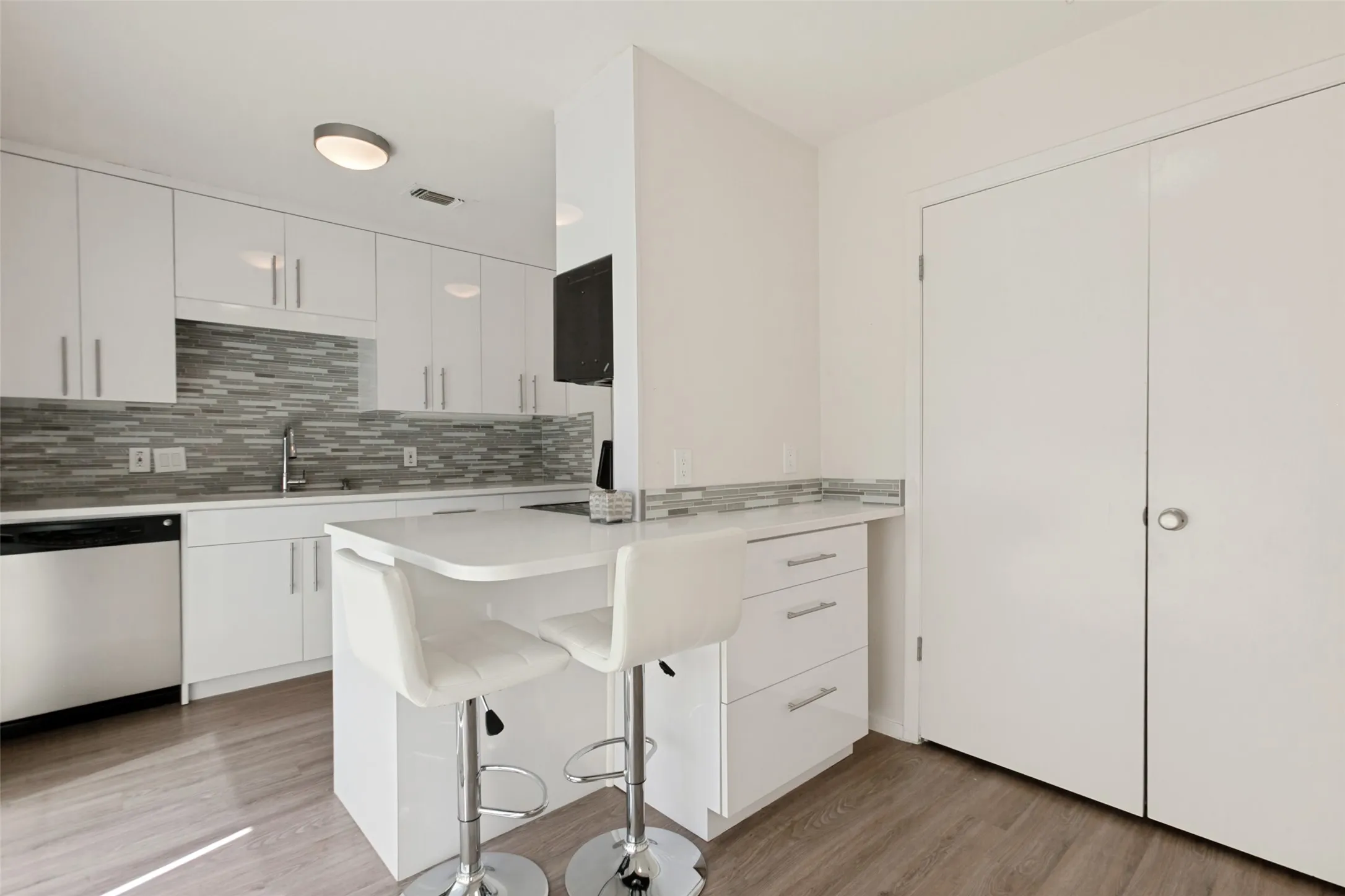 Kitchen featuring white cabinetry, a light-toned tile backsplash, stainless steel dishwasher, and wood-finish flooring