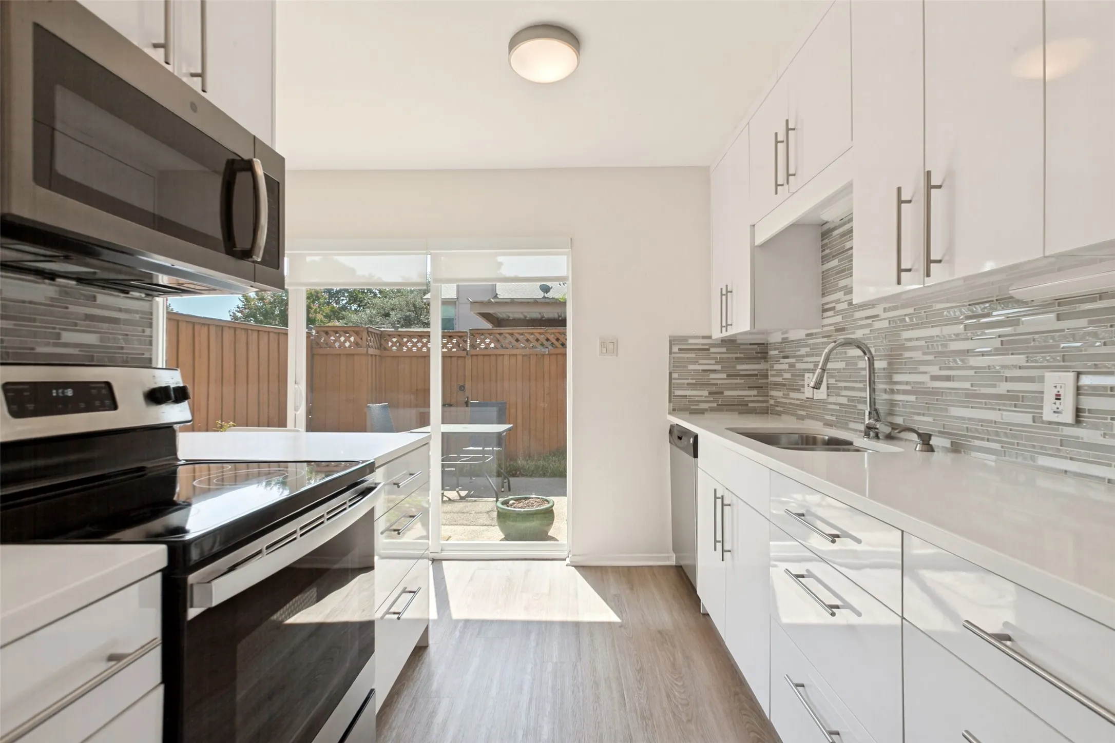 Sleek kitchen featuring white cabinetry, stainless steel appliances, mosaic tile backsplash, and wood-finish flooring