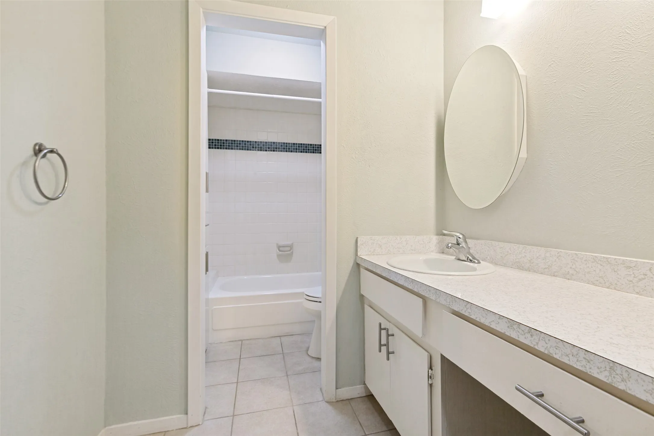 Bathroom featuring a vanity with an integrated sink, a wall-mounted mirror, and a tub with tiled walls