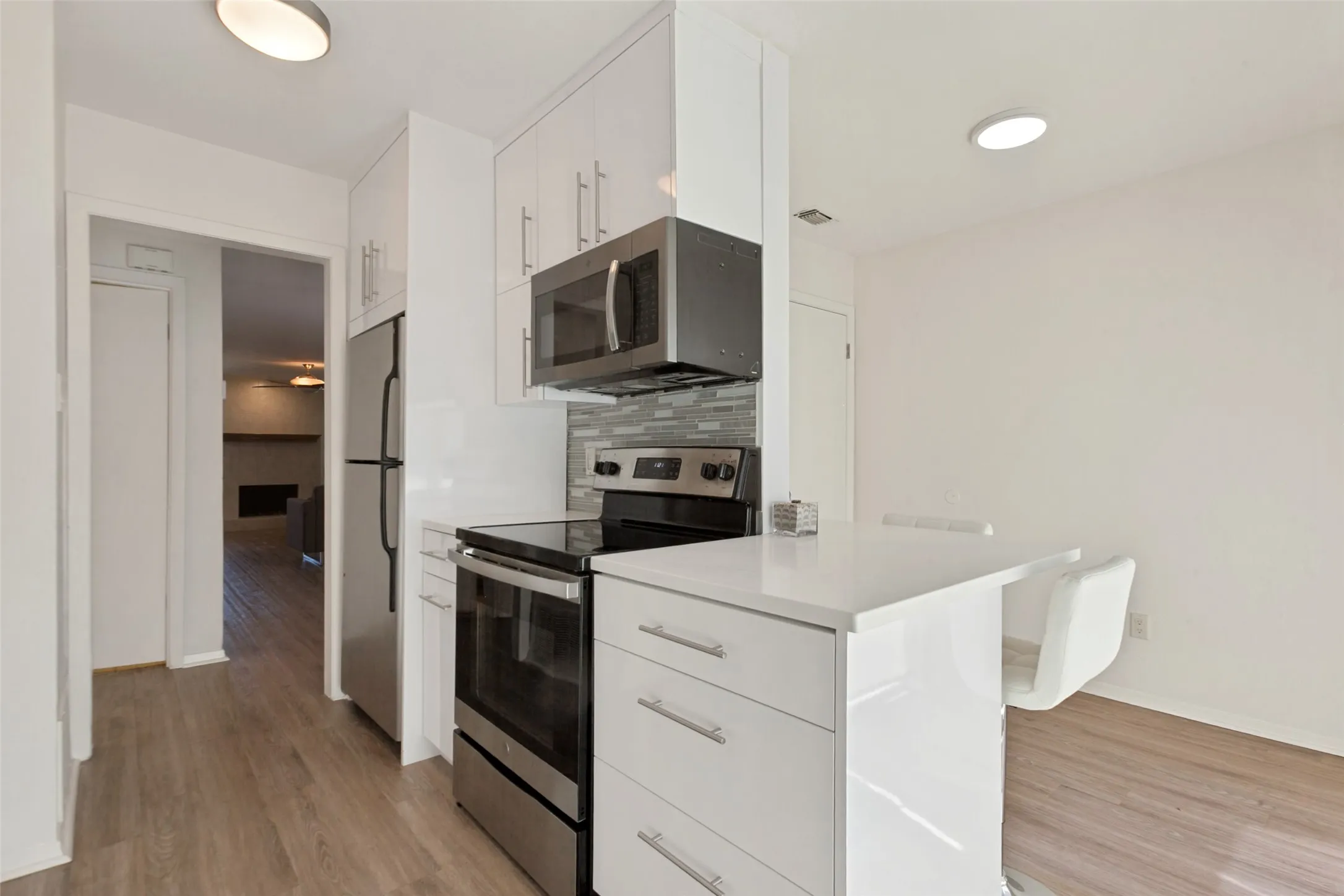 White cabinetry, stainless steel appliances, wood-finish flooring, white countertops, and a tile backsplash