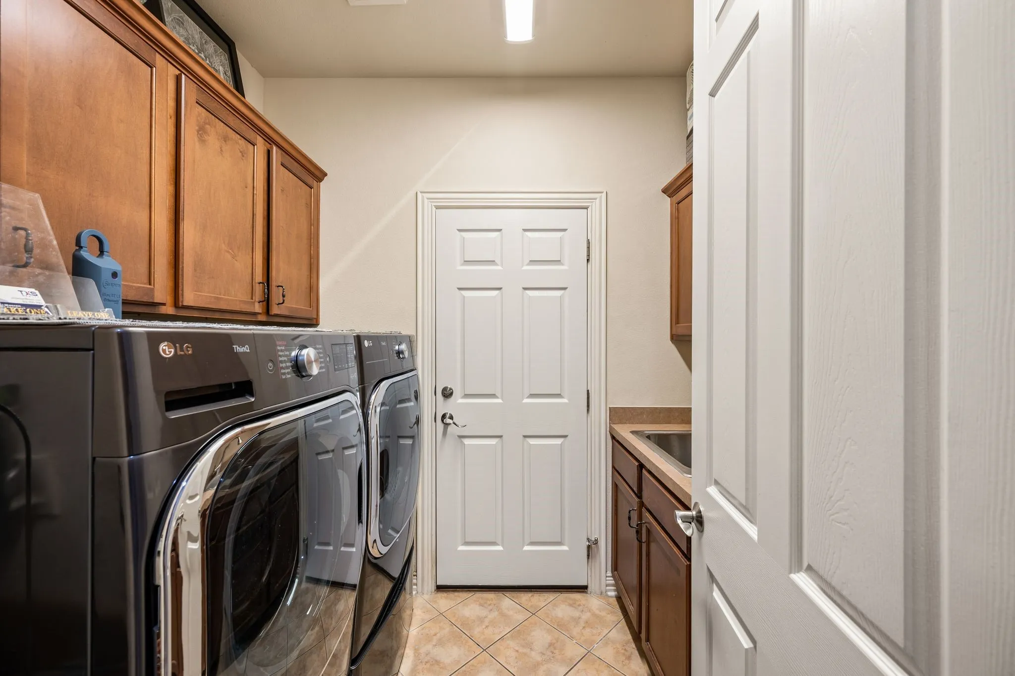Built-in wood-finish cabinetry, tiled flooring, white paneled door, and built-in sink with countertop
