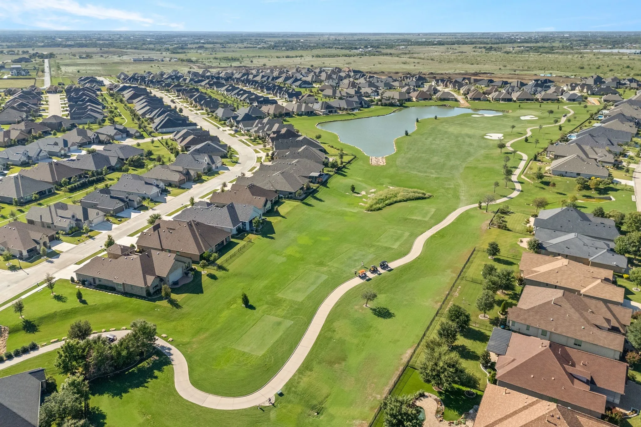 Expansive golf course setting featuring a water feature, paved cart paths, and manicured greens