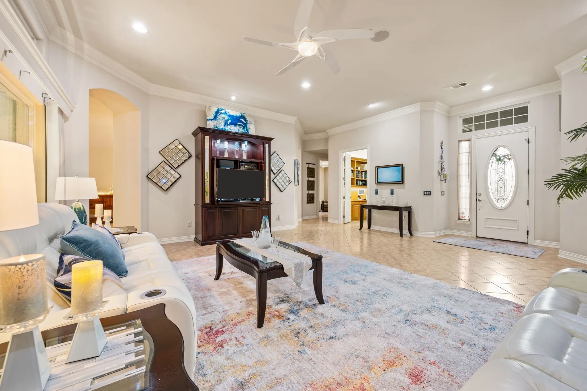 Recessed lighting, crown molding, a built-in entertainment center, a decorative front entry door with an oval glass insert, and tile flooring throughout