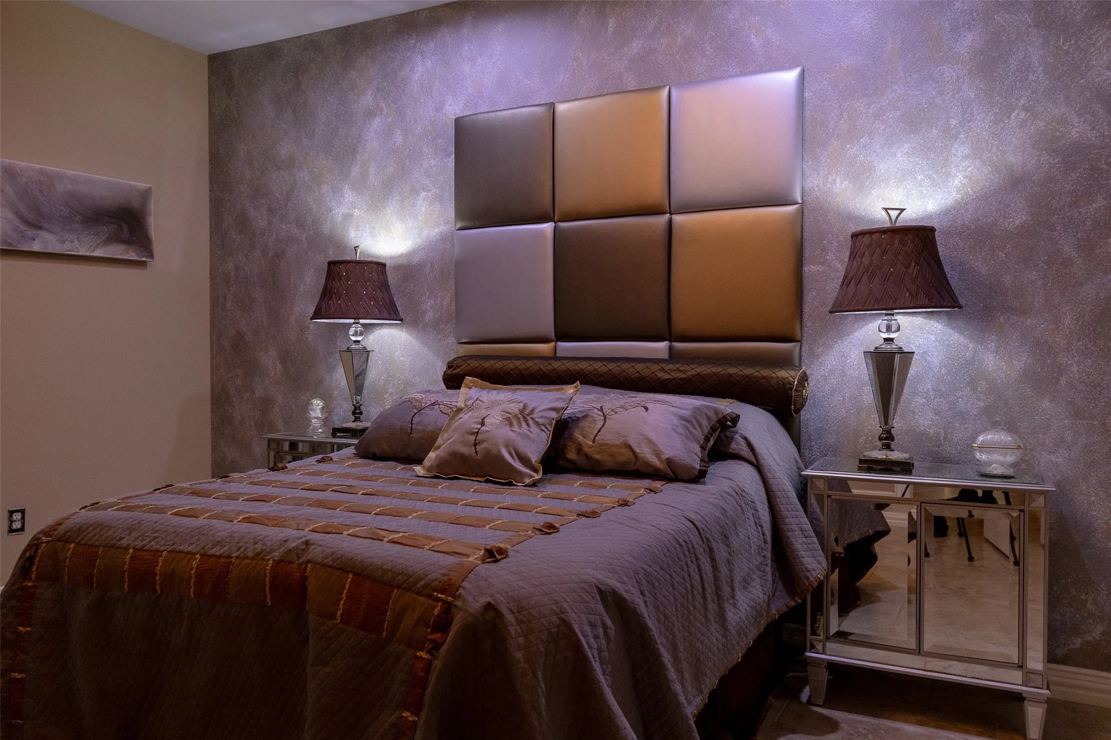 Textured accent wall, padded square panel headboard, mirrored nightstands, crystal-base table lamps, and upholstered bed frame
