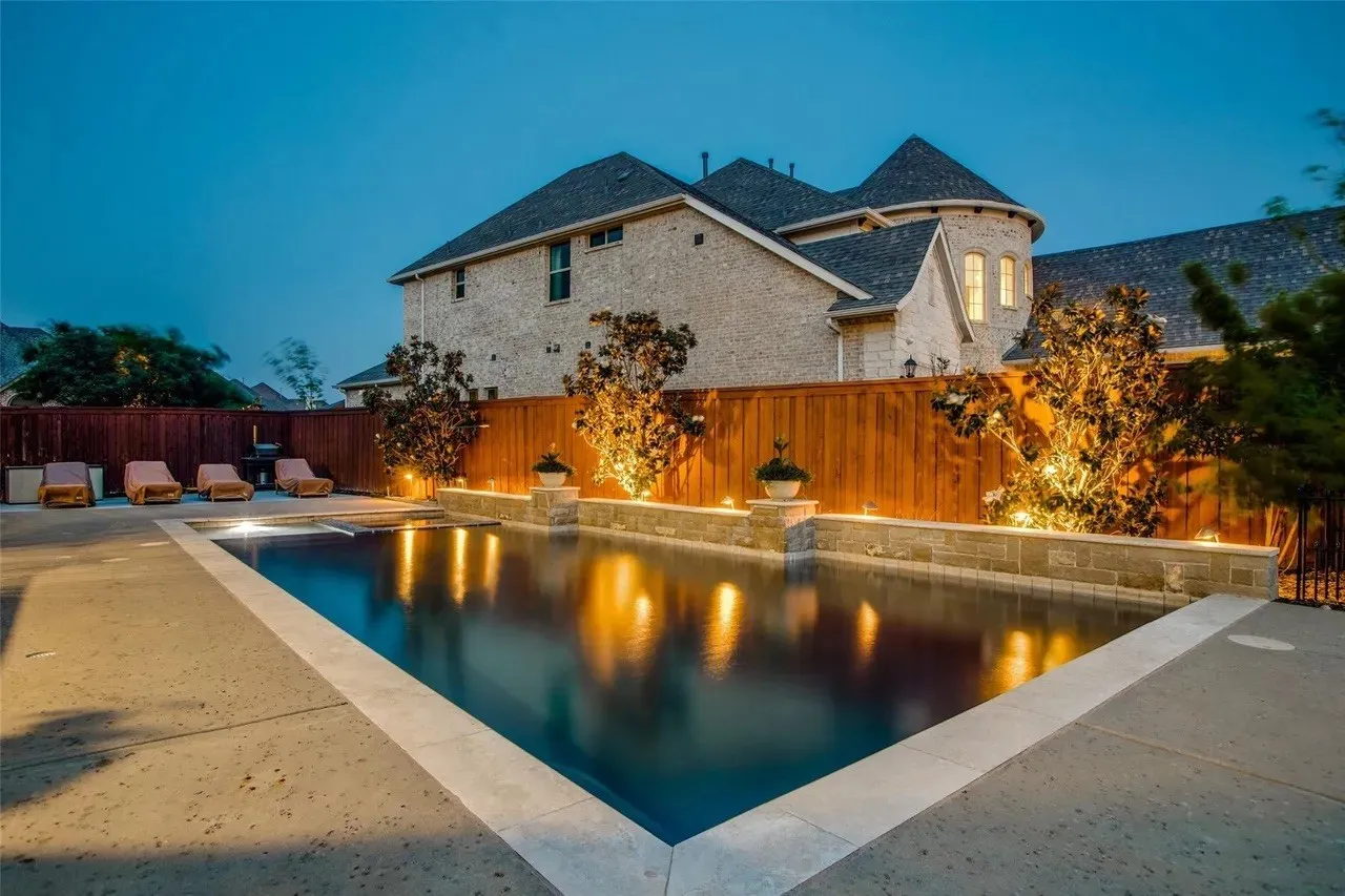 In-ground swimming pool with surrounding concrete decking, complemented by a stone retaining wall and a wood privacy fence