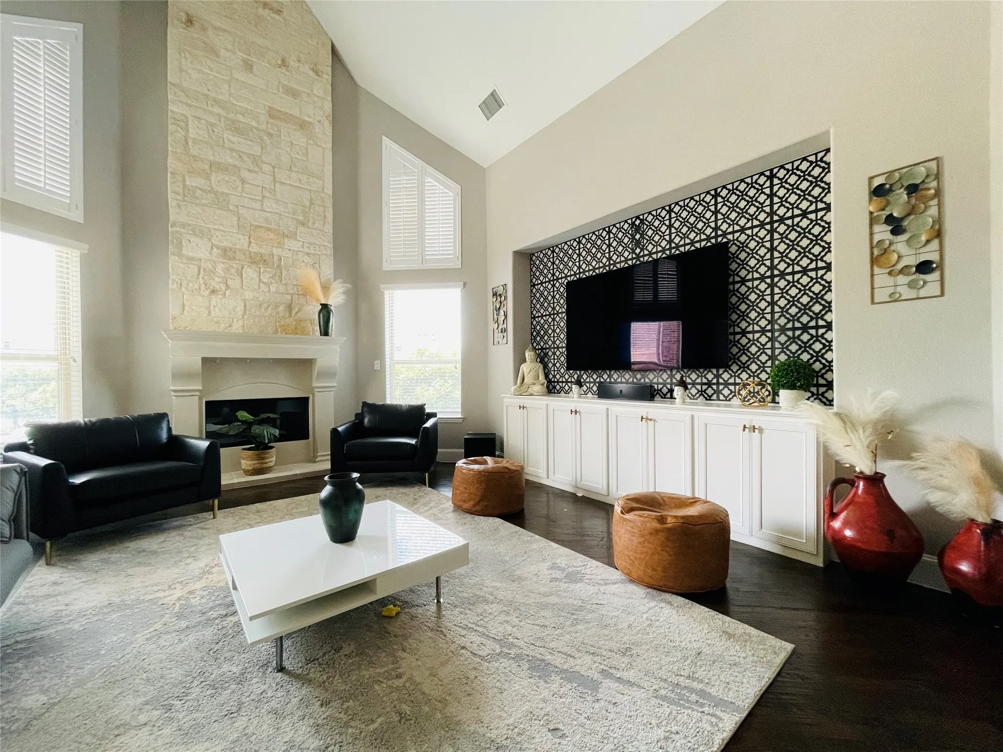 Vaulted ceilings with high windows, stone-clad fireplace, dark wood-finish flooring, and built-in cabinetry with decorative wall paneling