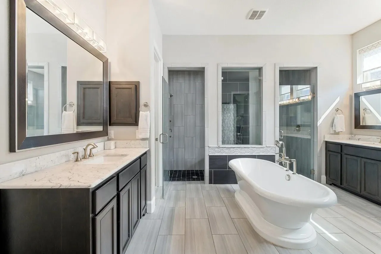 Dual vanities with white countertops, freestanding bathtub, and two walk-in showers with glass enclosures