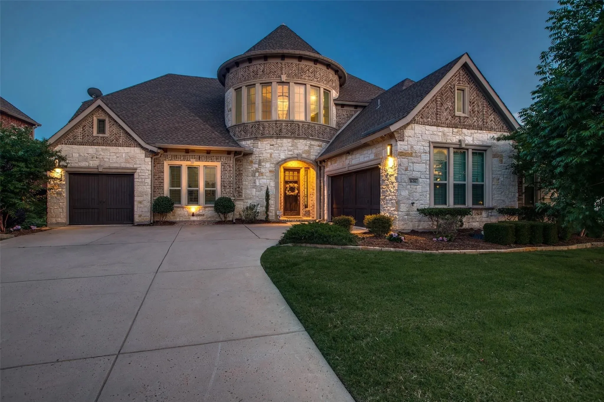 Stone and brick façade featuring a turret, arched entry, and dark garage doors