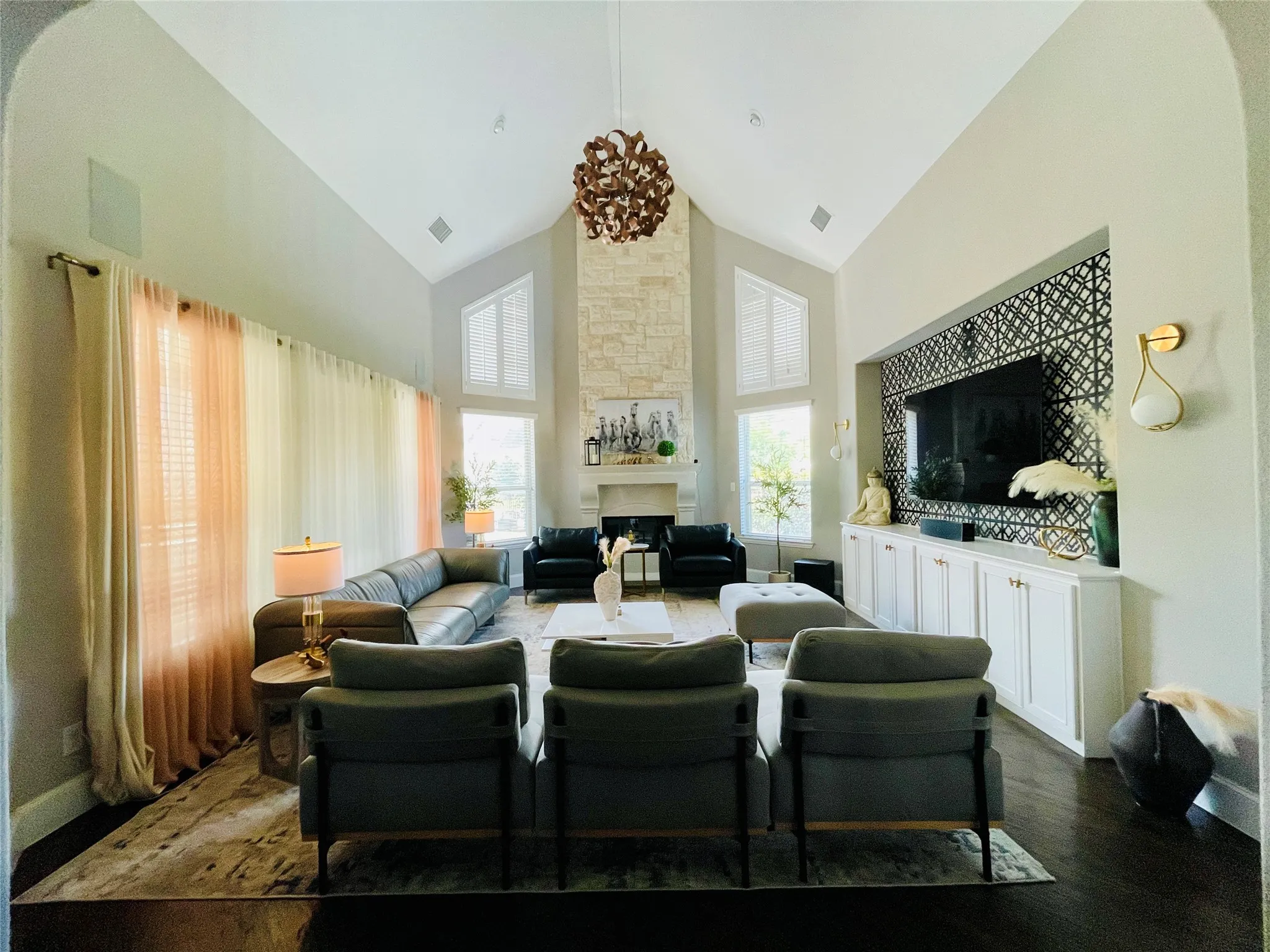 Vaulted ceilings, a stone-clad fireplace, integrated media built-ins, dark wood-finish flooring, and large windows with transom architectural details
