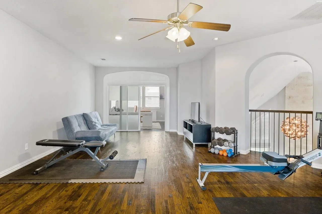 Hardwood-finish flooring, two arched doorways, ceiling fan with integrated lighting, recessed lighting, and a metal railing
