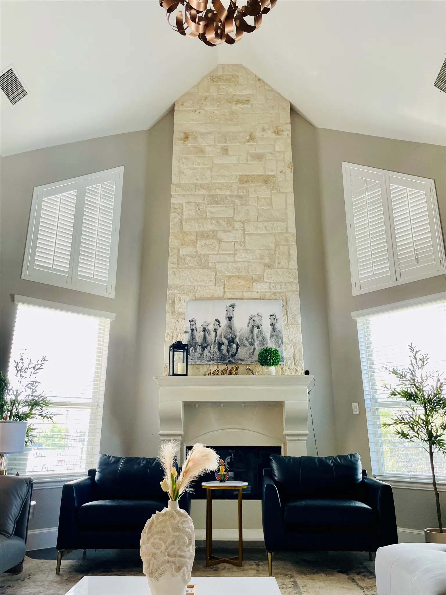 Stone-clad fireplace extending to a vaulted ceiling, flanked by multiple windows with plantation shutters