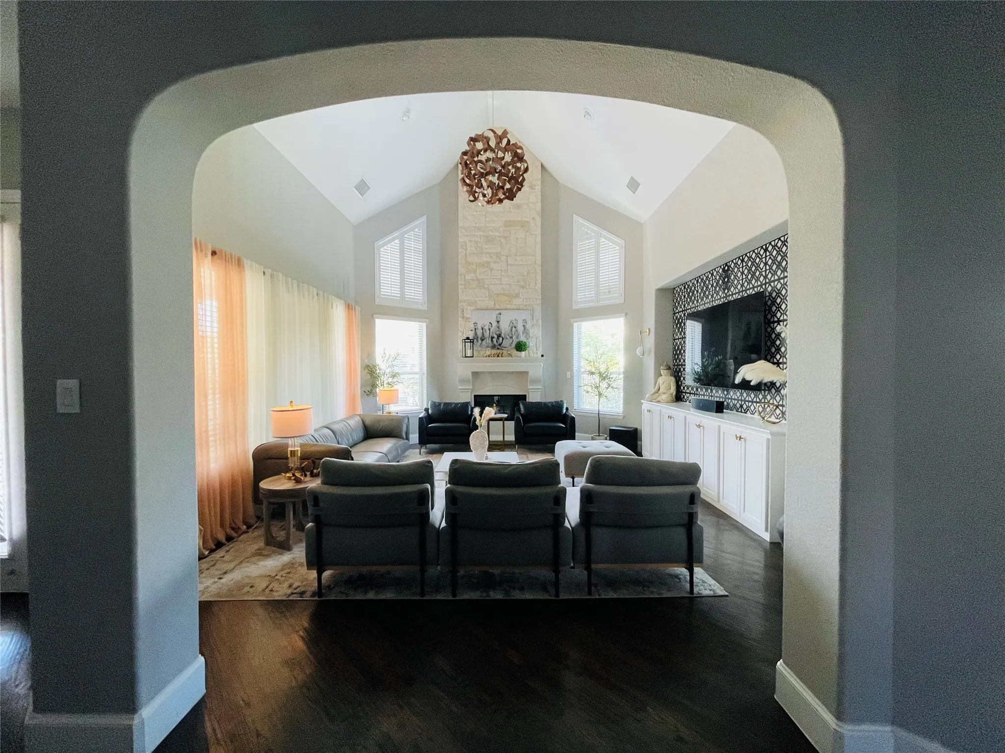 Spacious living area featuring a vaulted ceiling, stone-clad fireplace, dark wood-finish flooring, and built-in cabinetry with patterned tile detailing