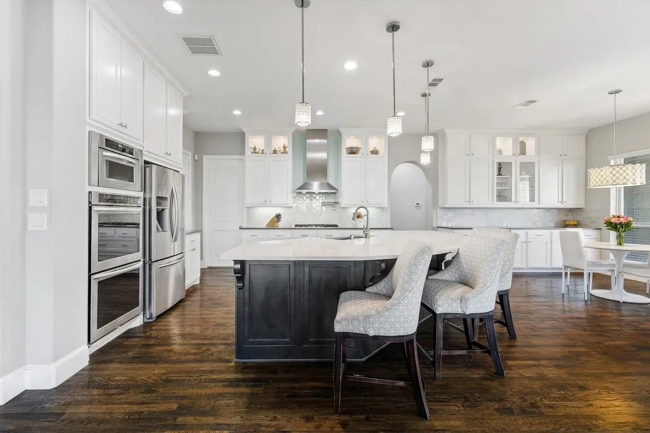 Gourmet kitchen with stainless steel appliances, a center island featuring pendant lighting, white upper and lower cabinetry, and wood-finish flooring