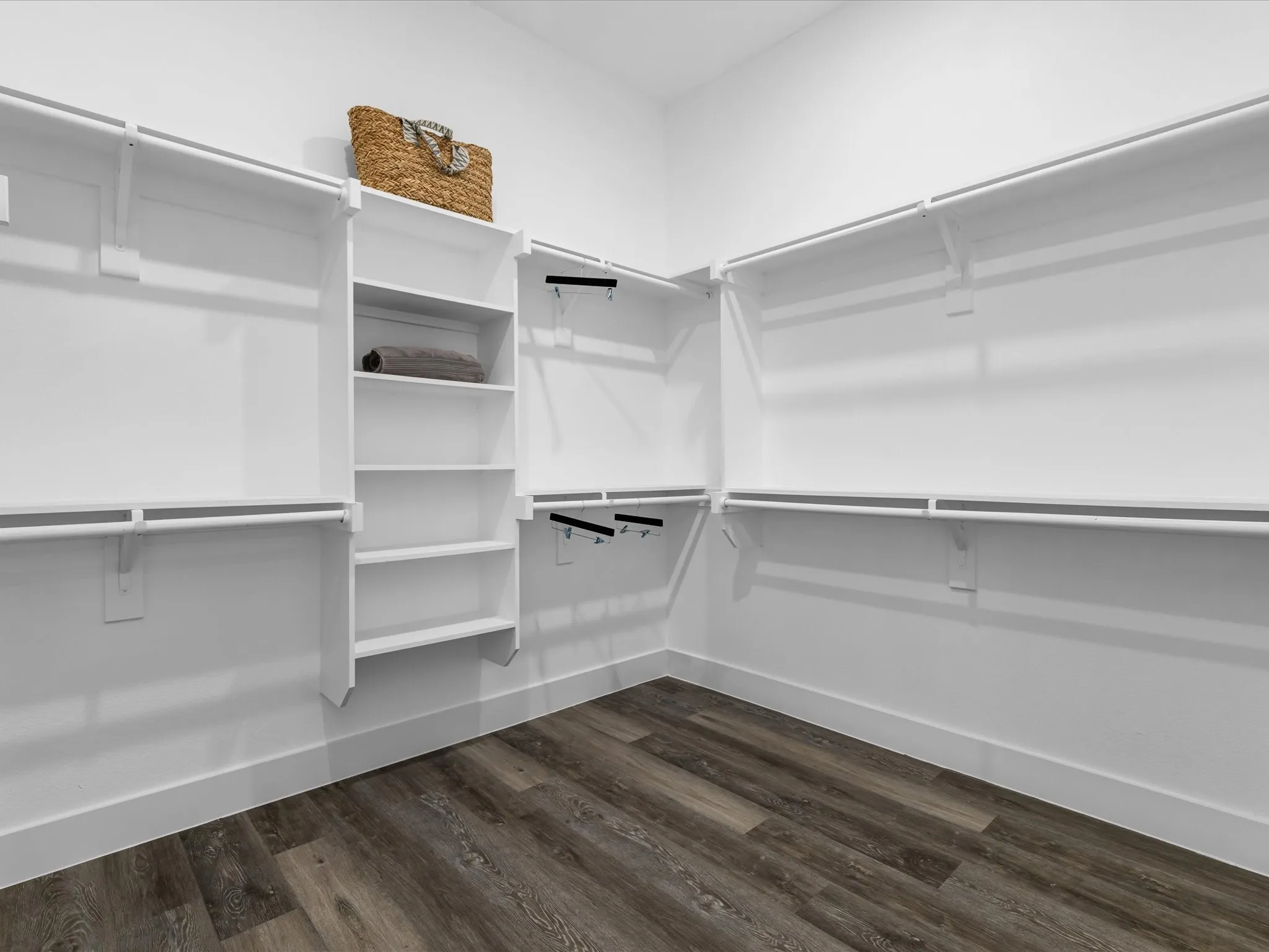 Spacious closet with wood-finish flooring, white built-in shelving, and multiple hanging rods