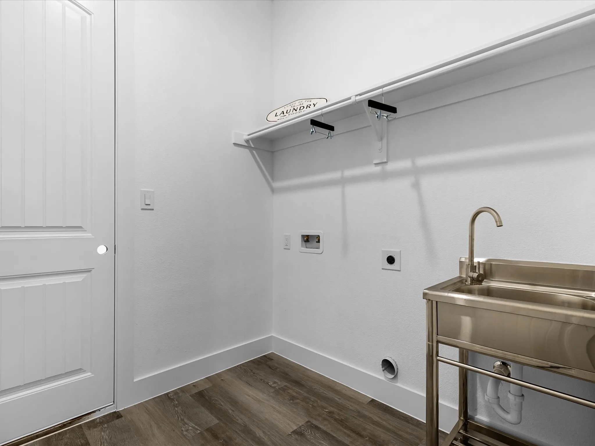 Utility room featuring wood-finish flooring, a white paneled door, built-in shelving, and a stainless steel utility sink with a gooseneck faucet