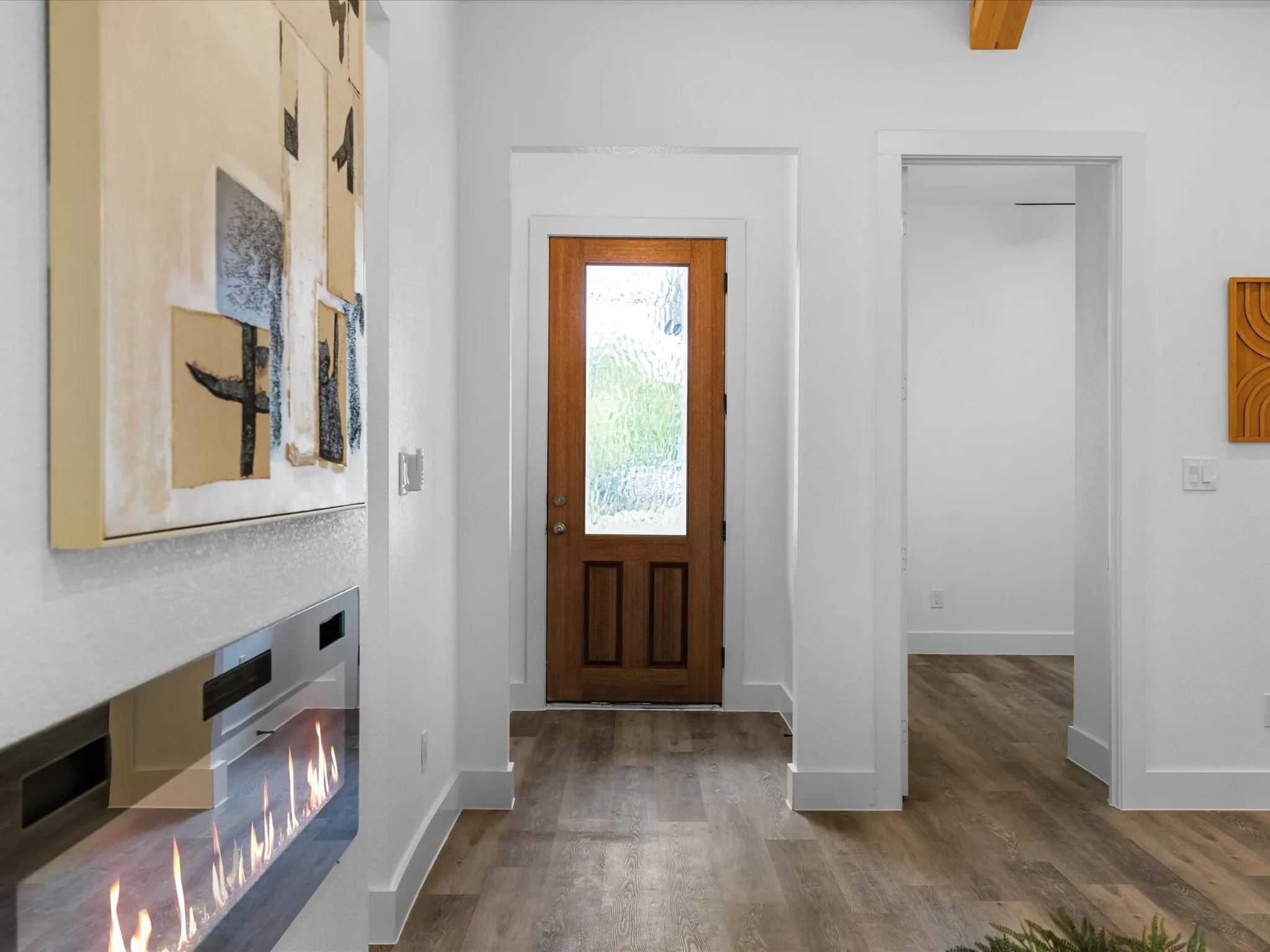 Wood-finish flooring, white walls, exposed beam, wood entry door with privacy glass, and linear electric fireplace