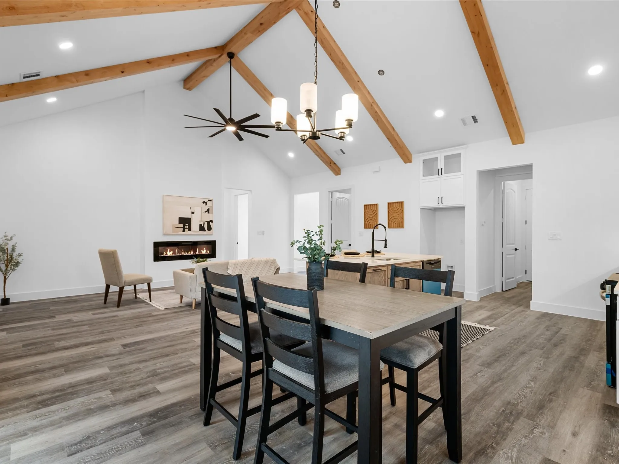 Vaulted ceiling with exposed wood beams, wood-finish flooring, built-in electric fireplace, recessed lighting, and a kitchen island with a single-basin sink and matte black faucet