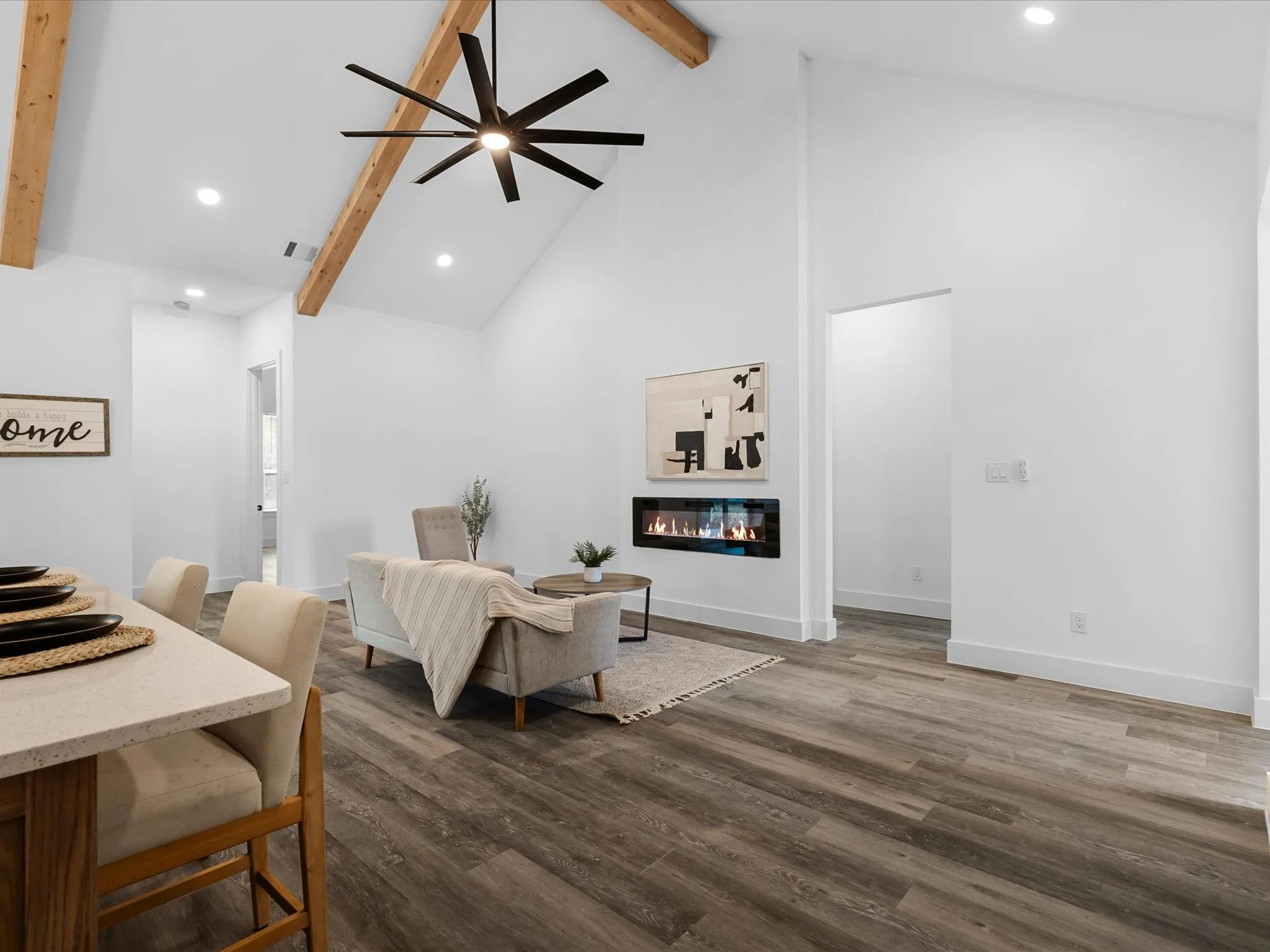 Vaulted ceiling with exposed wood beams, wood-finish flooring, recessed lighting, built-in linear fireplace, and a contemporary ceiling fan