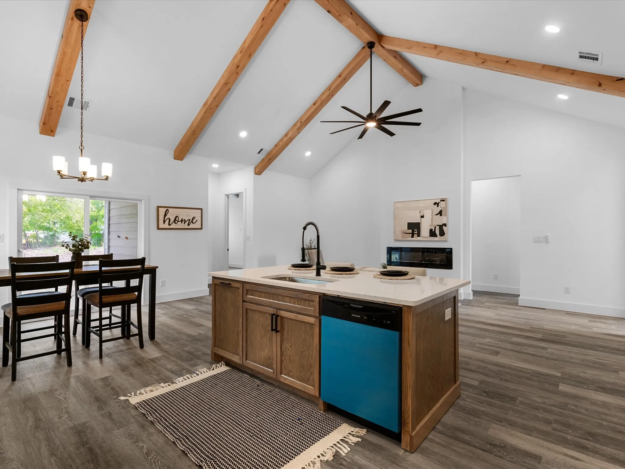 Vaulted ceiling with exposed wood beams, wood-finish flooring, island with integrated sink, built-in fireplace, and sliding glass door