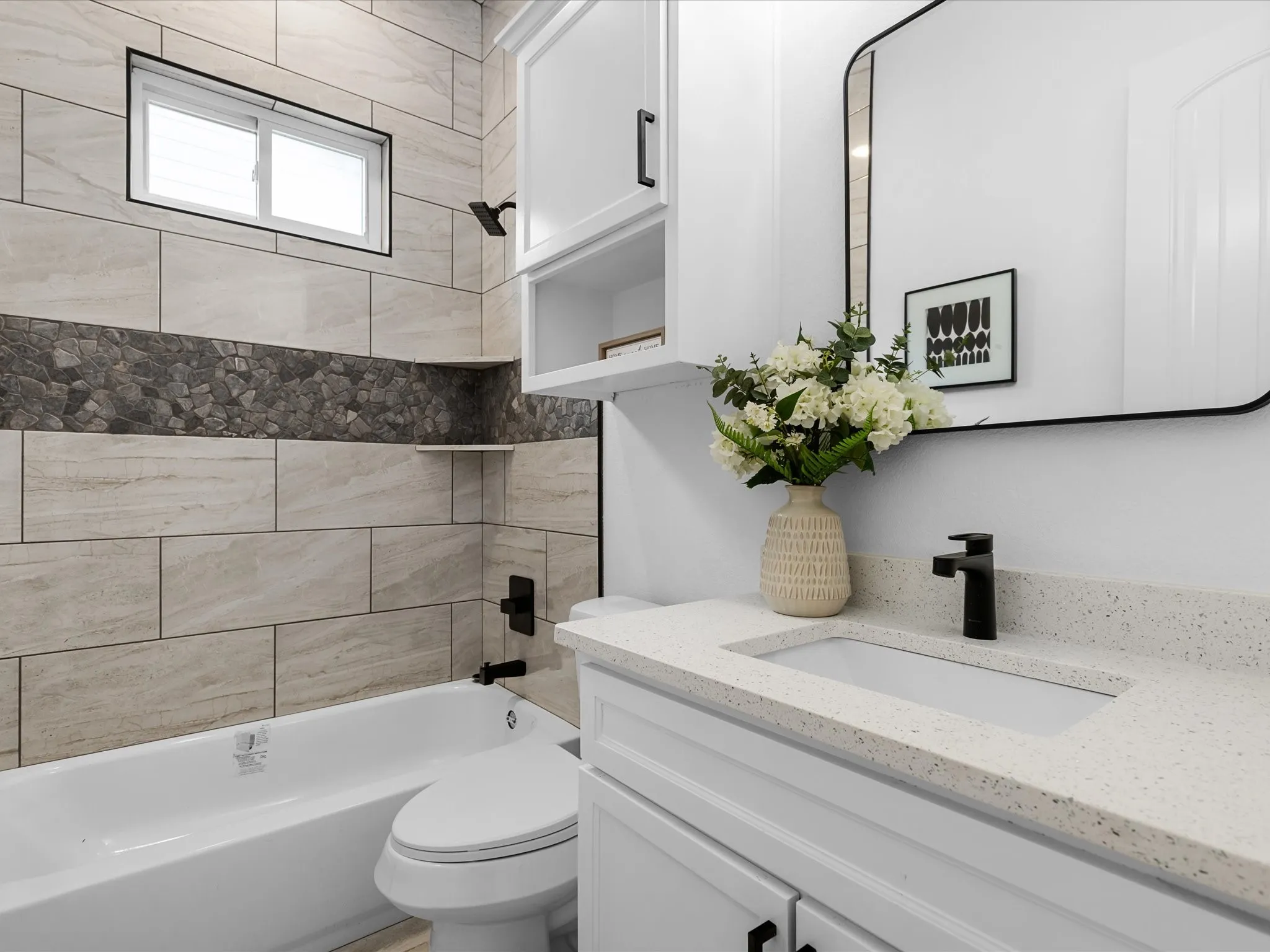 White vanity with a speckled countertop and integrated sink, matte black faucet, and a rectangular framed mirror
