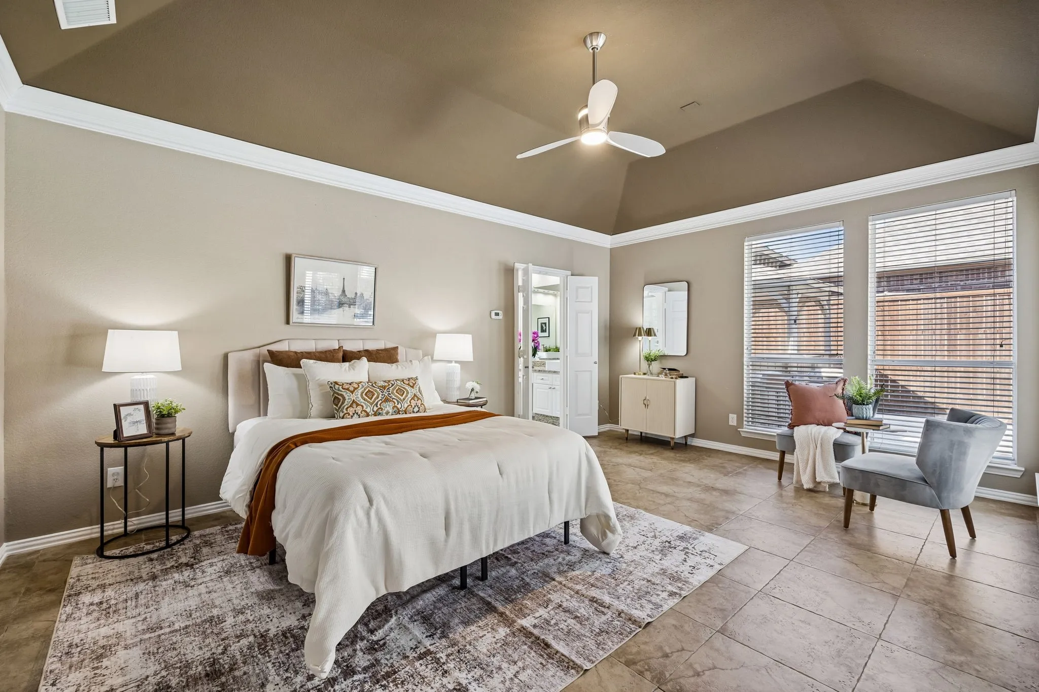 Vaulted ceiling with crown molding, ceiling fan, tile flooring, and a pair of tall windows with blinds