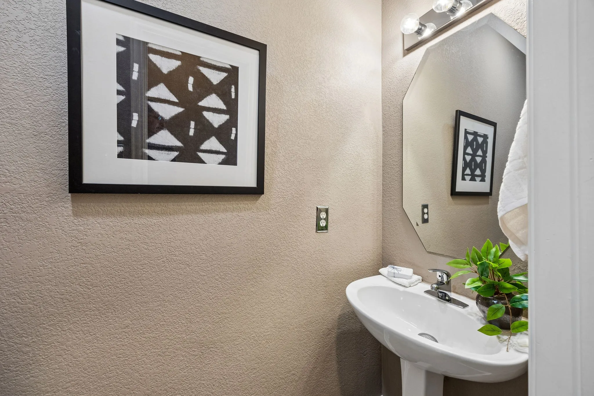 Pedestal sink with chrome faucet, octagonal mirror, and vanity lighting