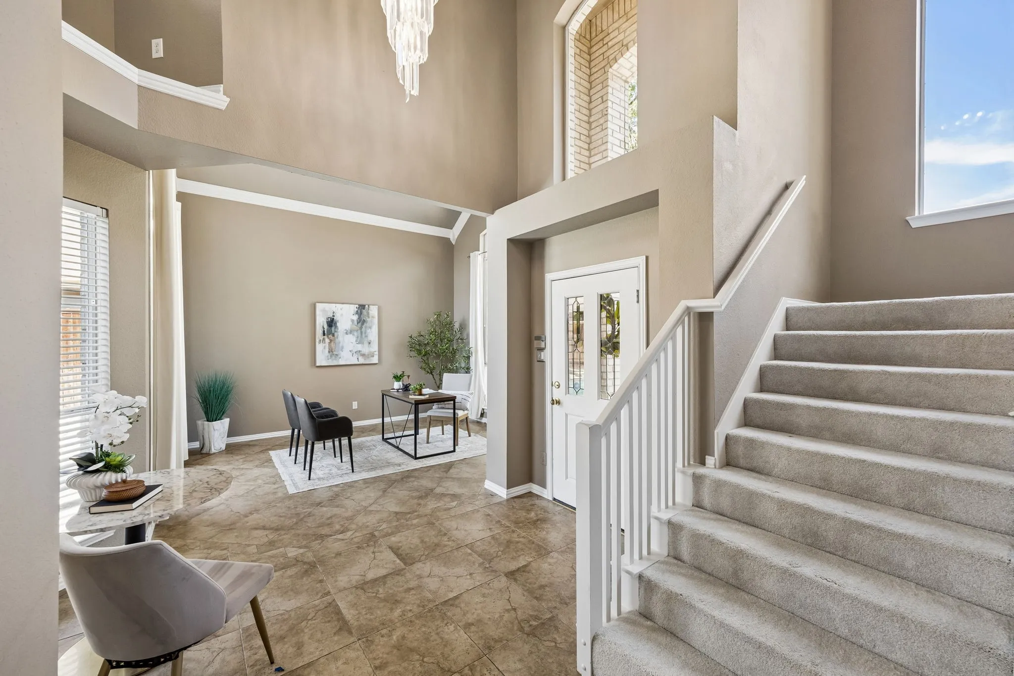 Two-story foyer with high ceilings, tile flooring, a carpeted staircase with white railings, and a transom window above the entry door