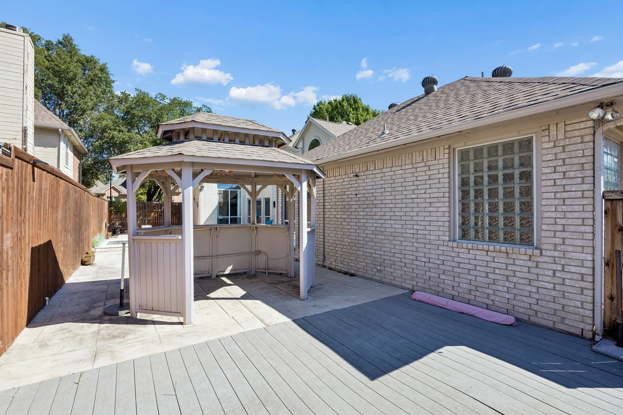 Spacious outdoor decking with a dedicated gazebo structure, brick exterior, and glass block window