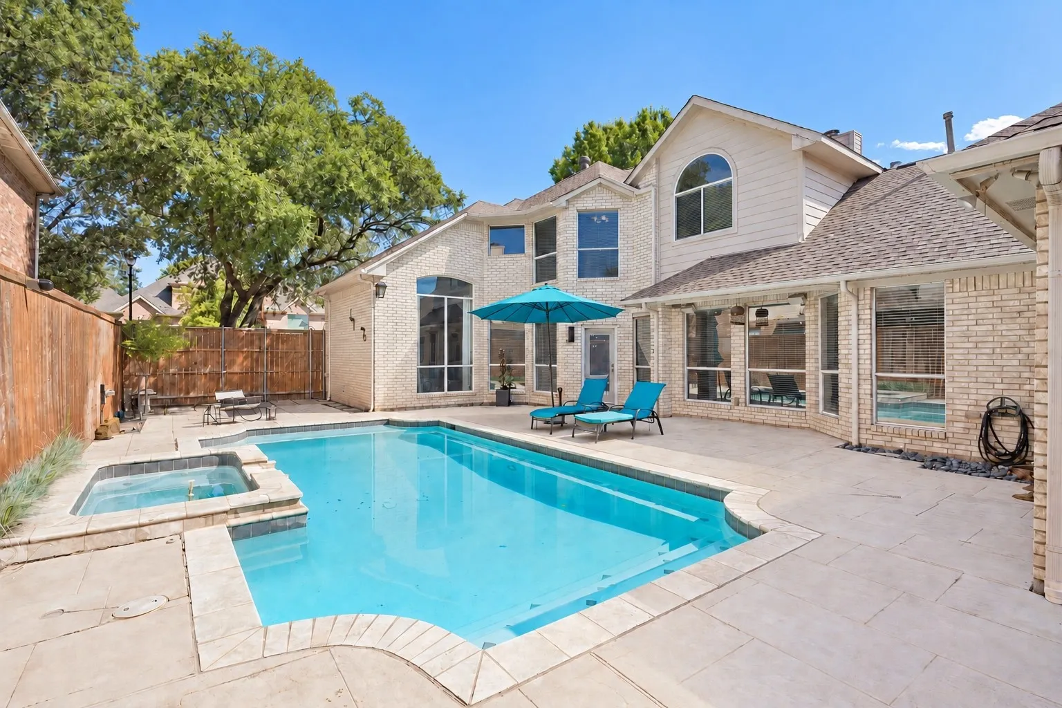 Expansive outdoor living area featuring a rectangular swimming pool, integrated spa, and light-toned patio pavers