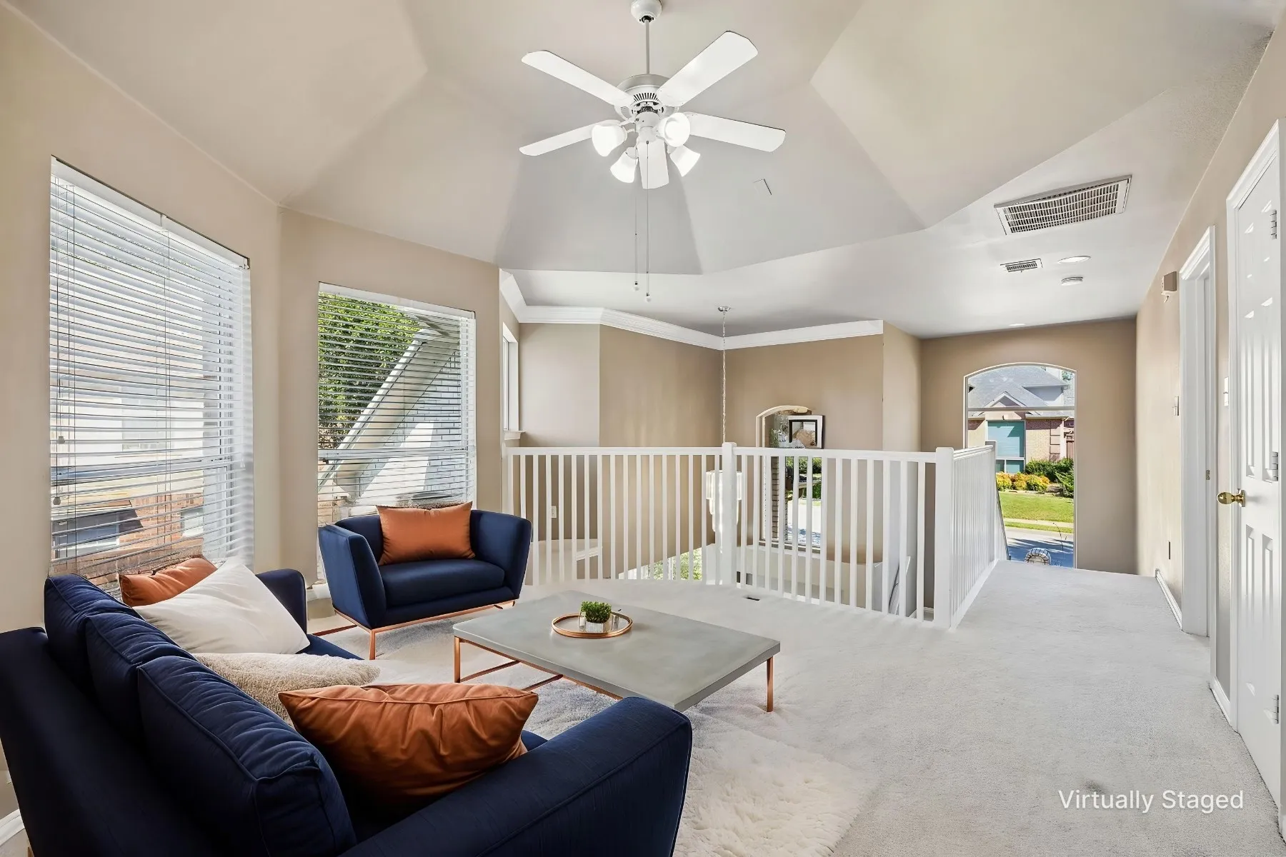 Vaulted ceiling with a ceiling fan, white spindle railing, arched doorway, two windows with blinds, and light-toned carpeting