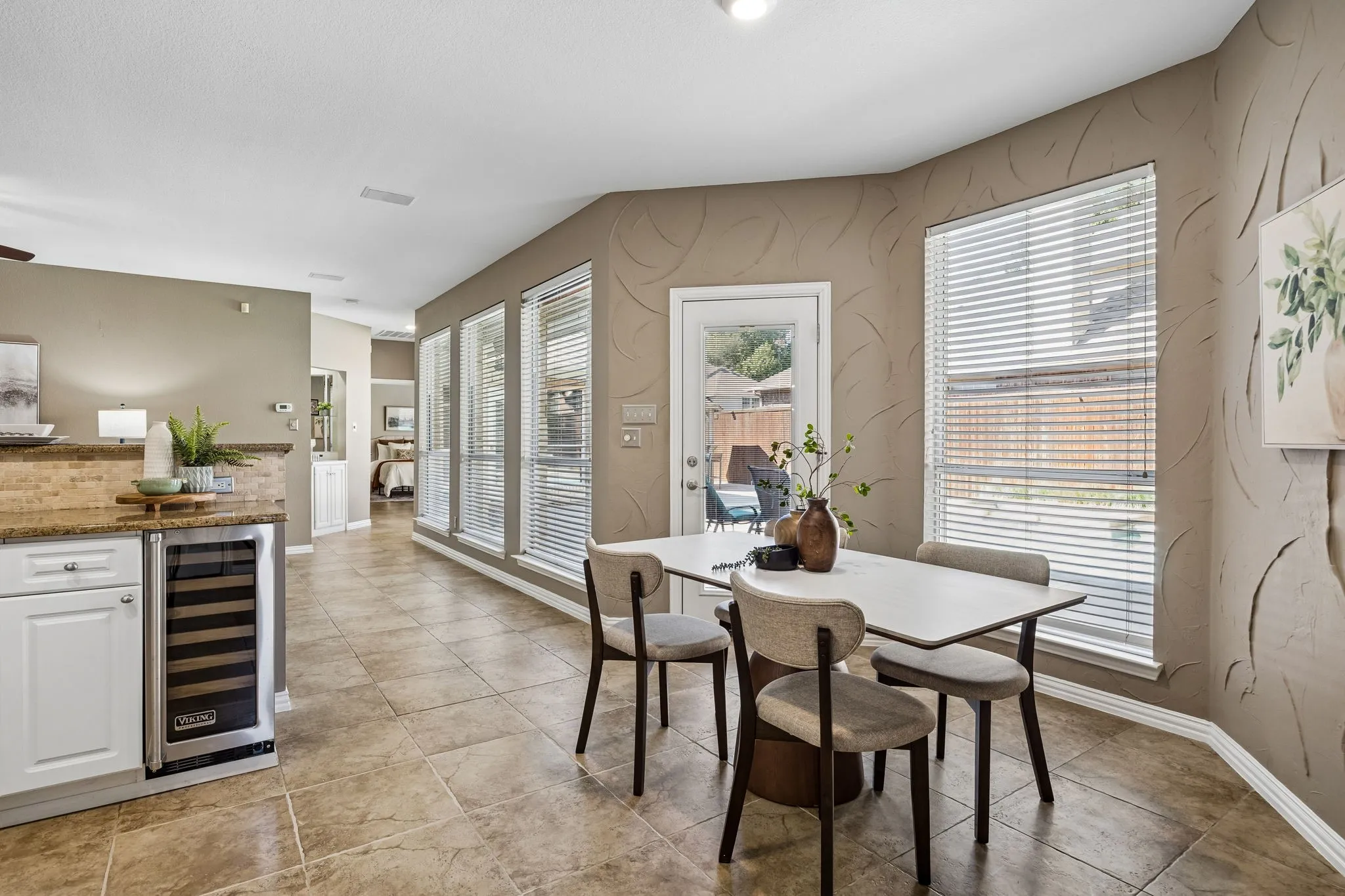 Tile flooring, built-in beverage cooler, white cabinetry, granite-style countertops, and multiple windows with blinds