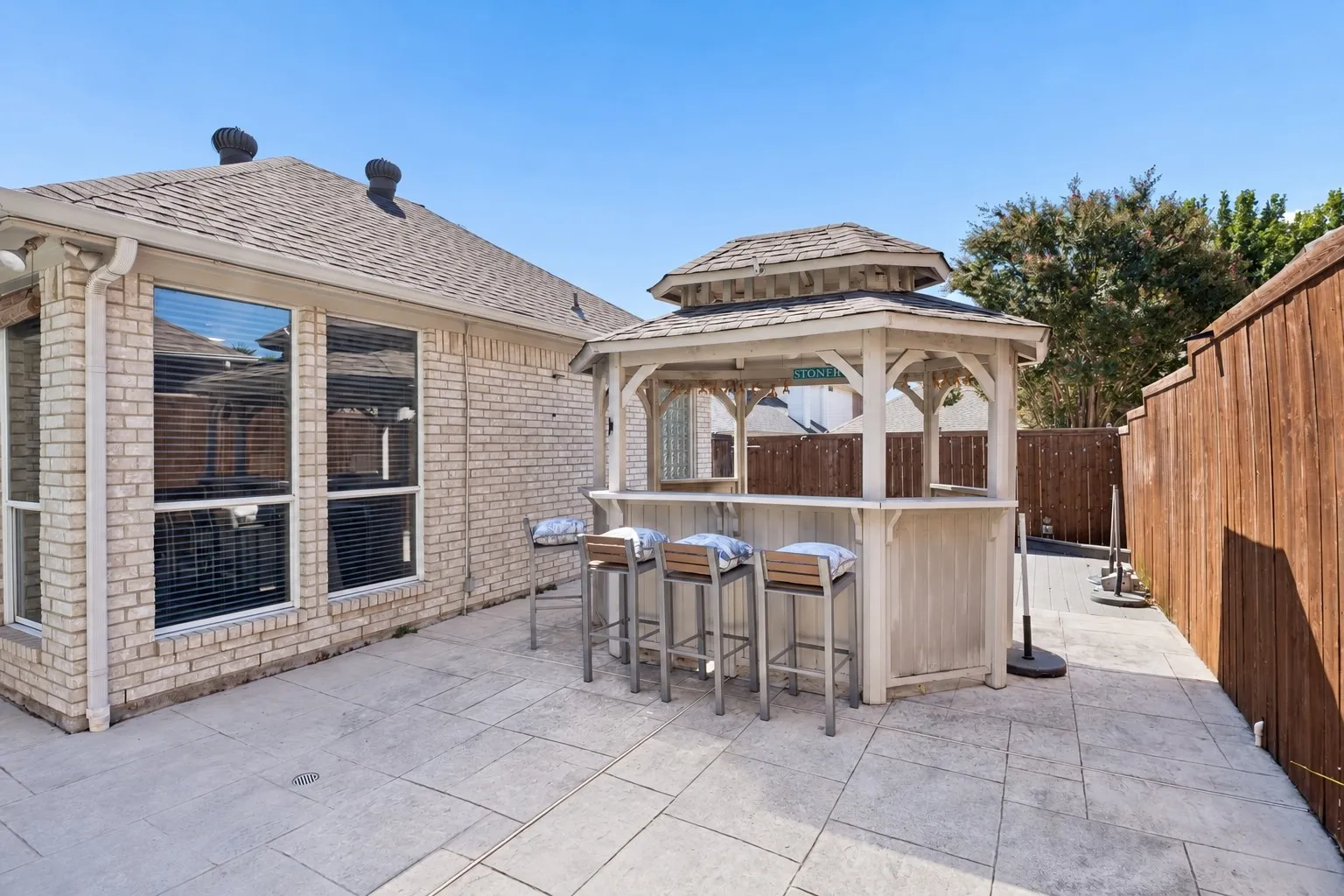 Spacious paver patio featuring a built-in gazebo bar, a brick exterior, and a wood privacy fence