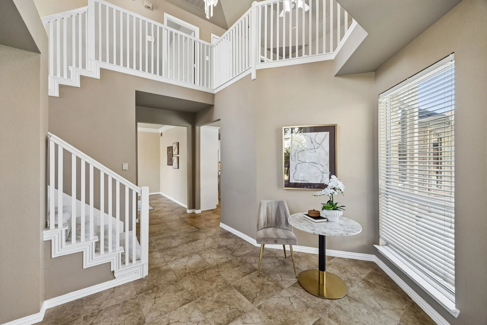 Two-story entry featuring a white spindle staircase, upper-level railing, and neutral tile flooring